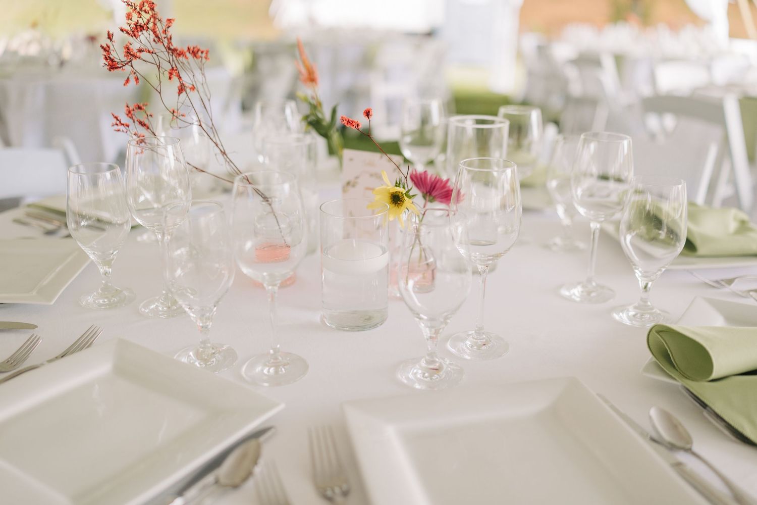 Elegant wedding reception table settings with white linens, crystal glassware, and delicate floral centerpieces.
