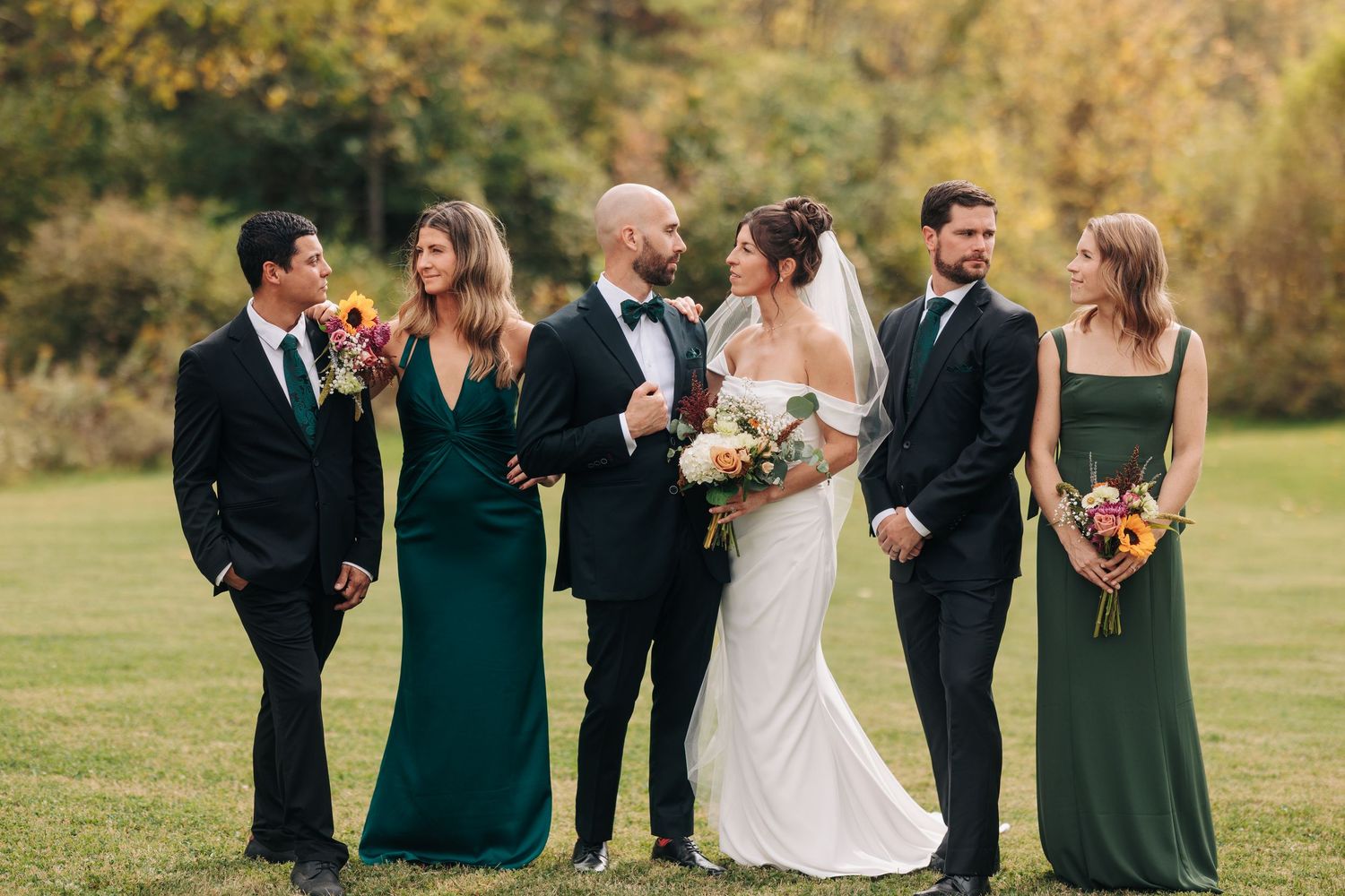 Wedding party poses for formal portraits on a sunny autumn day with golden foliage.