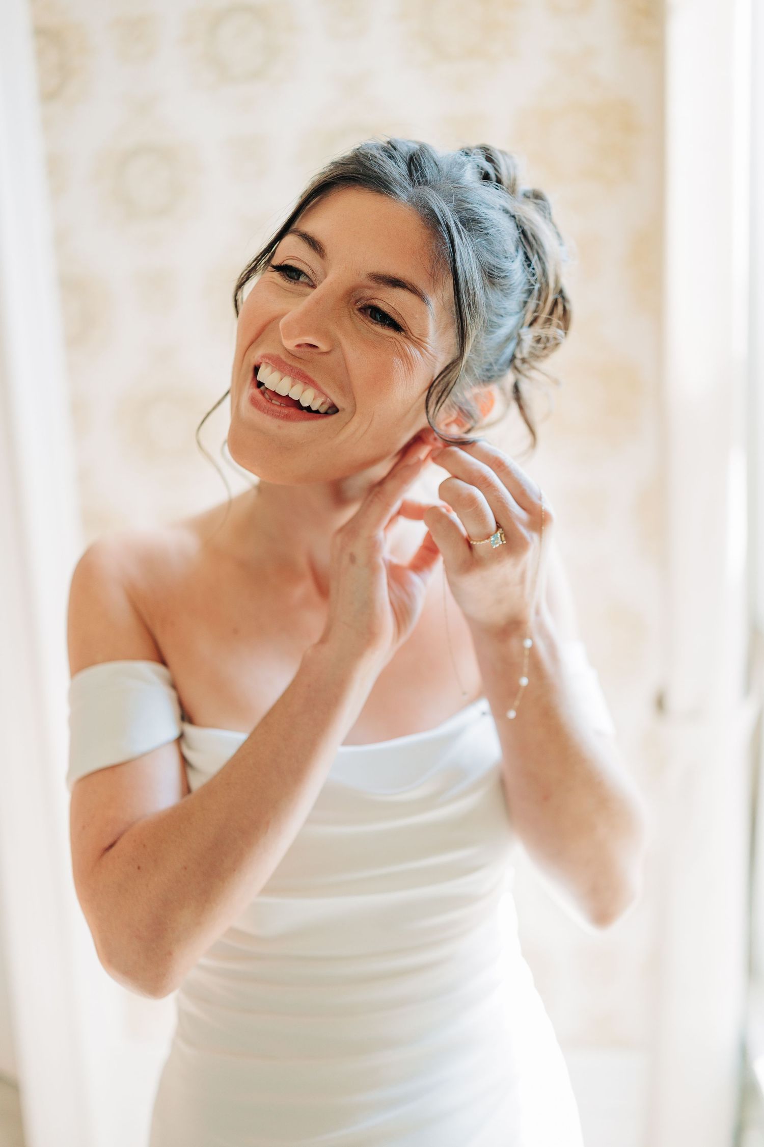 A joyful person with blue hair wearing a white top laughs while talking on the phone in a bright setting.