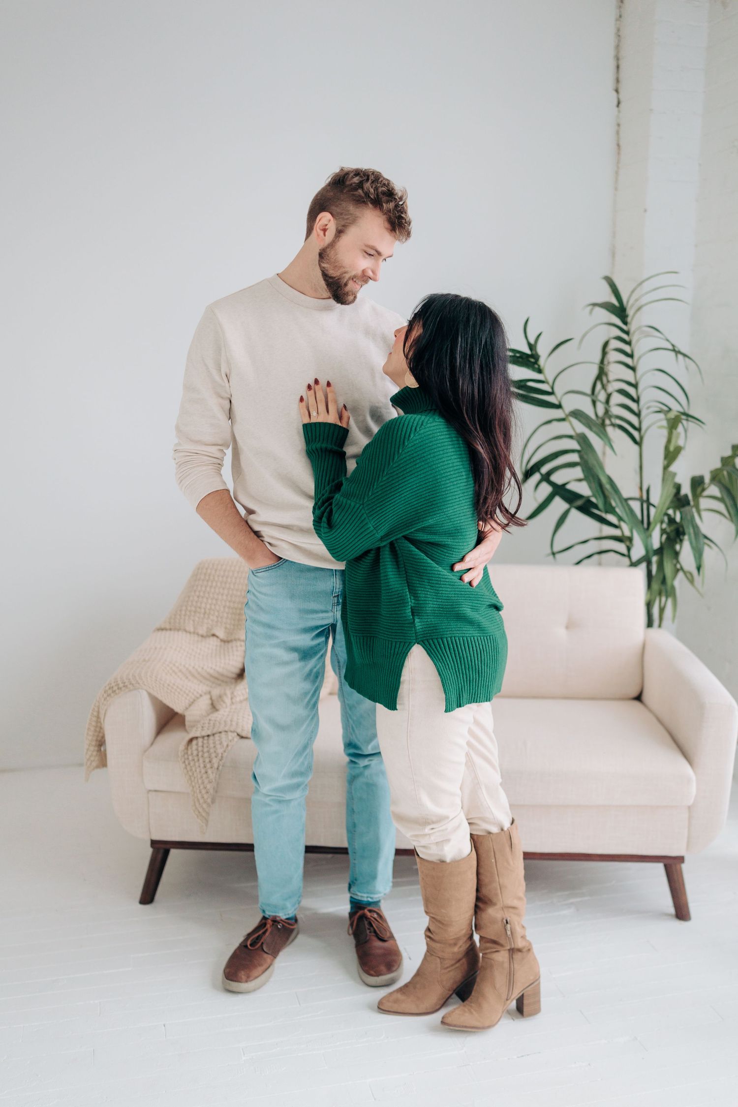 A couple in casual attire sits together on a white couch with a green plant in the background.