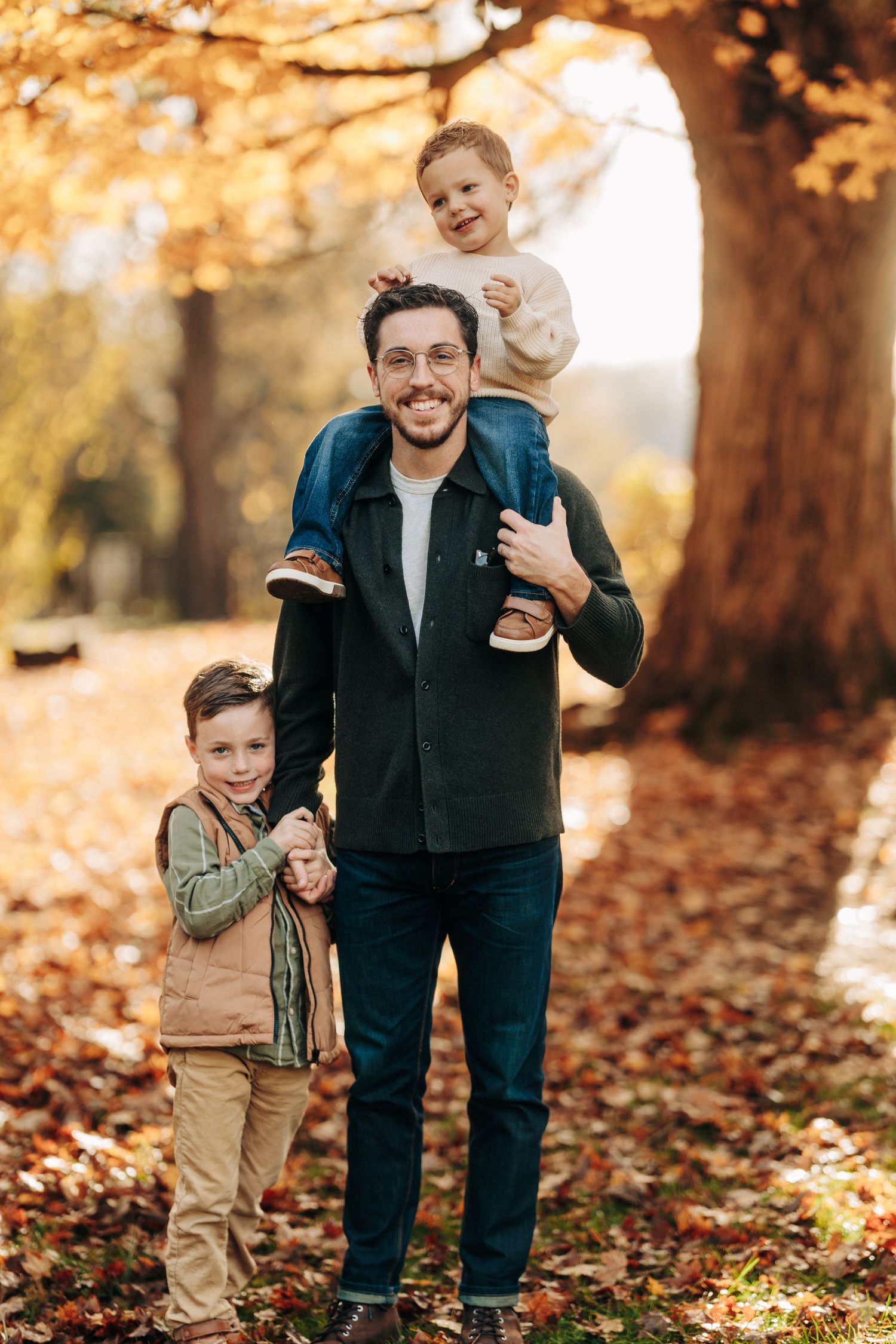 Family enjoying an autumn day together in a park with fallen leaves and golden sunlight filtering through trees.