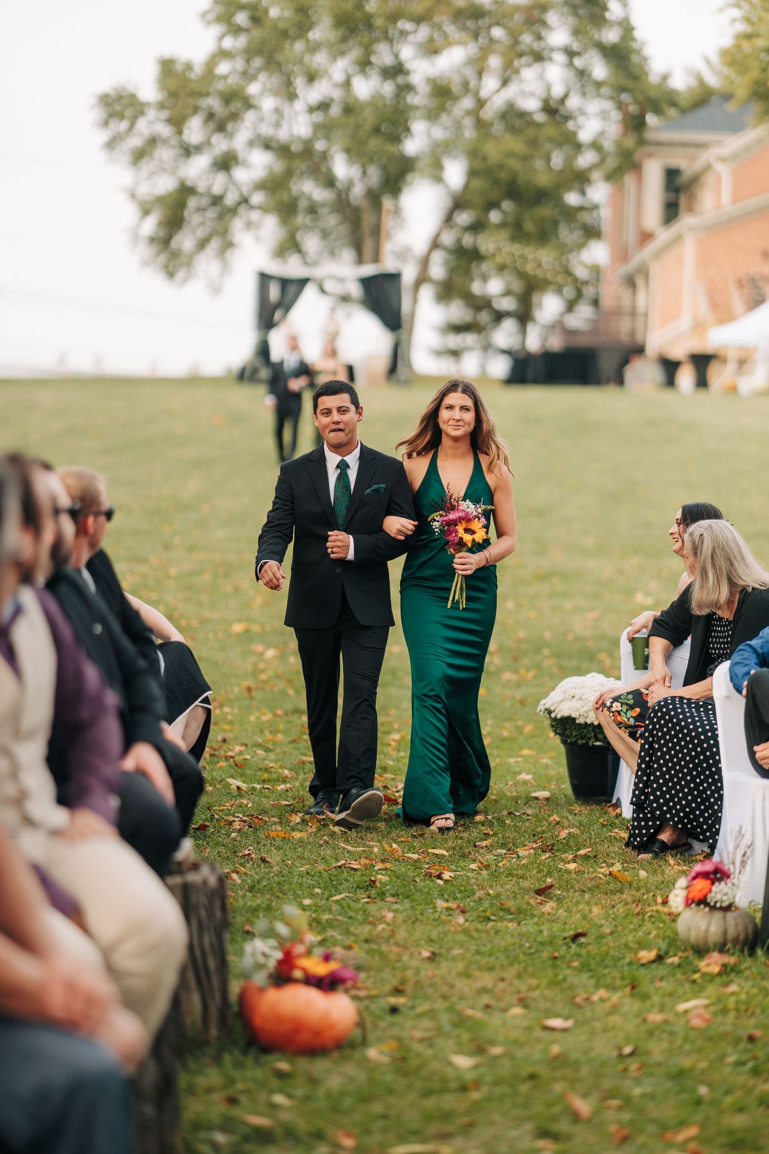 Wedding guests walking across lawn with autumn leaves and pumpkin decorations.
