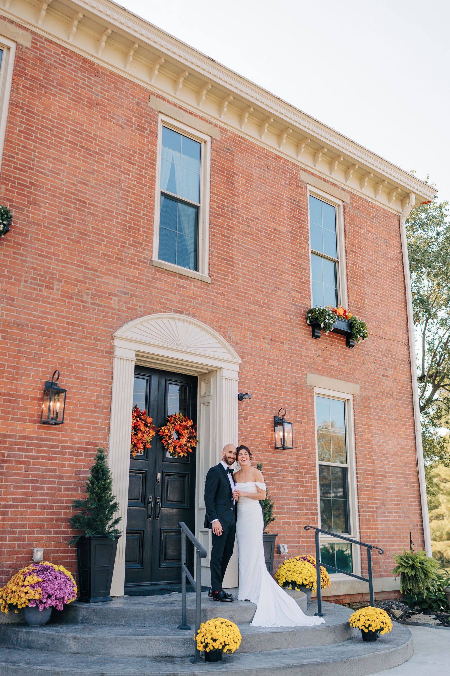 Classic brick wedding venue entrance decorated with fall flowers and black lanterns.