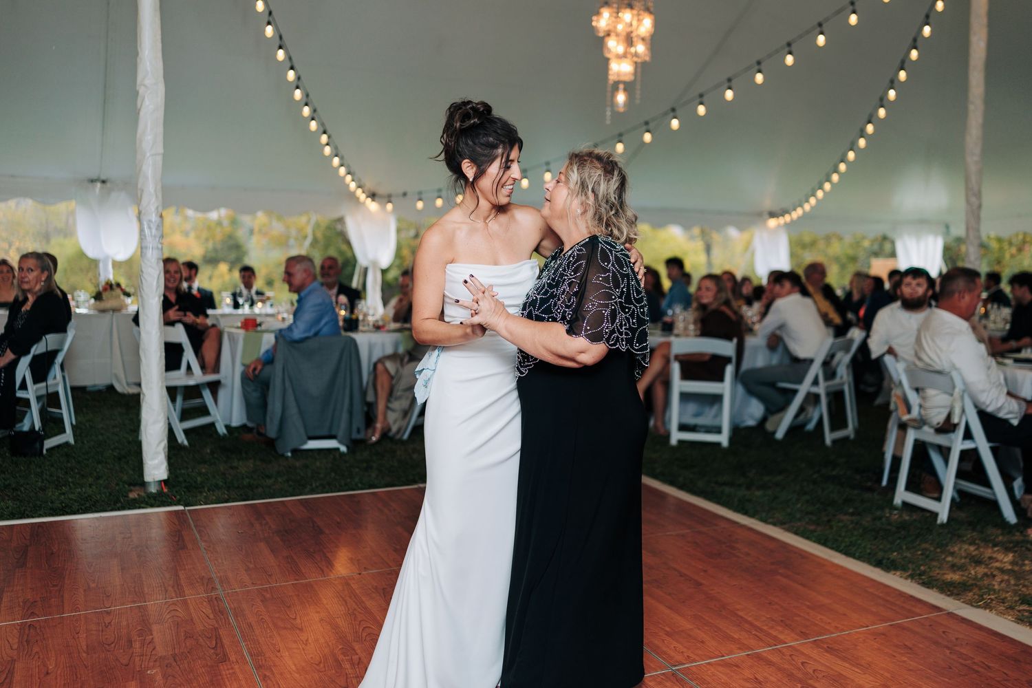A wedding reception under a tent with string lights and guests seated at tables.