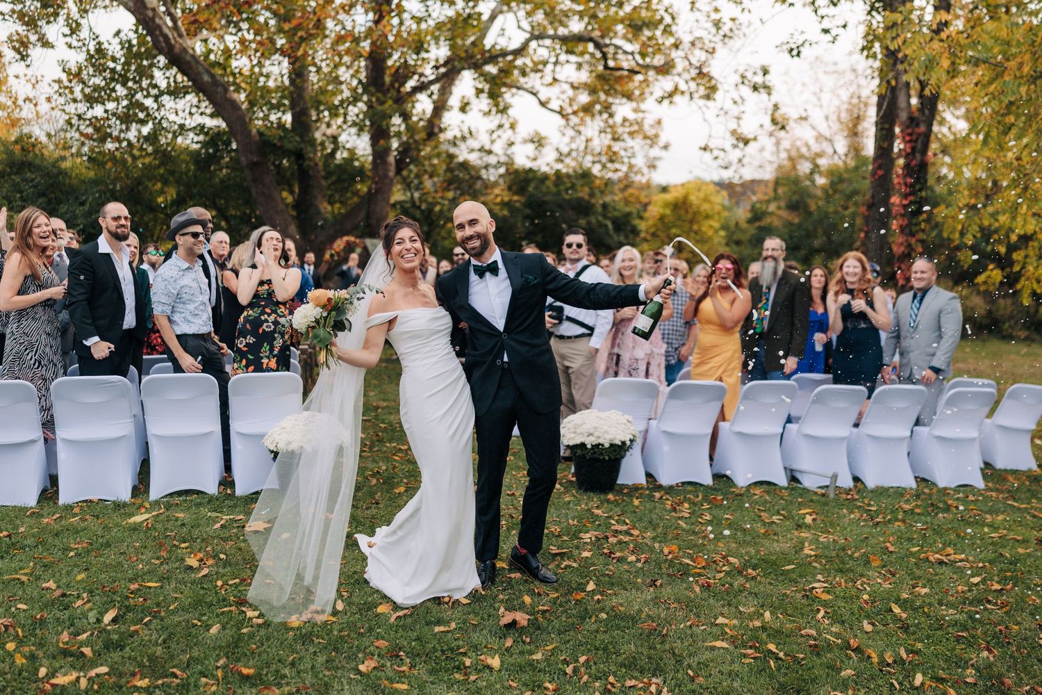 Panoramic view of an outdoor wedding ceremony with white chairs and autumn trees.