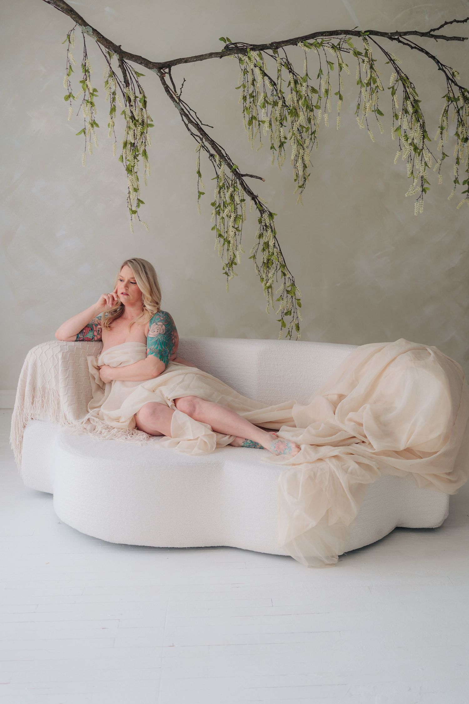 Artistic maternity photo series showing a pregnant woman in white fabric against a light backdrop with hanging willow branches.