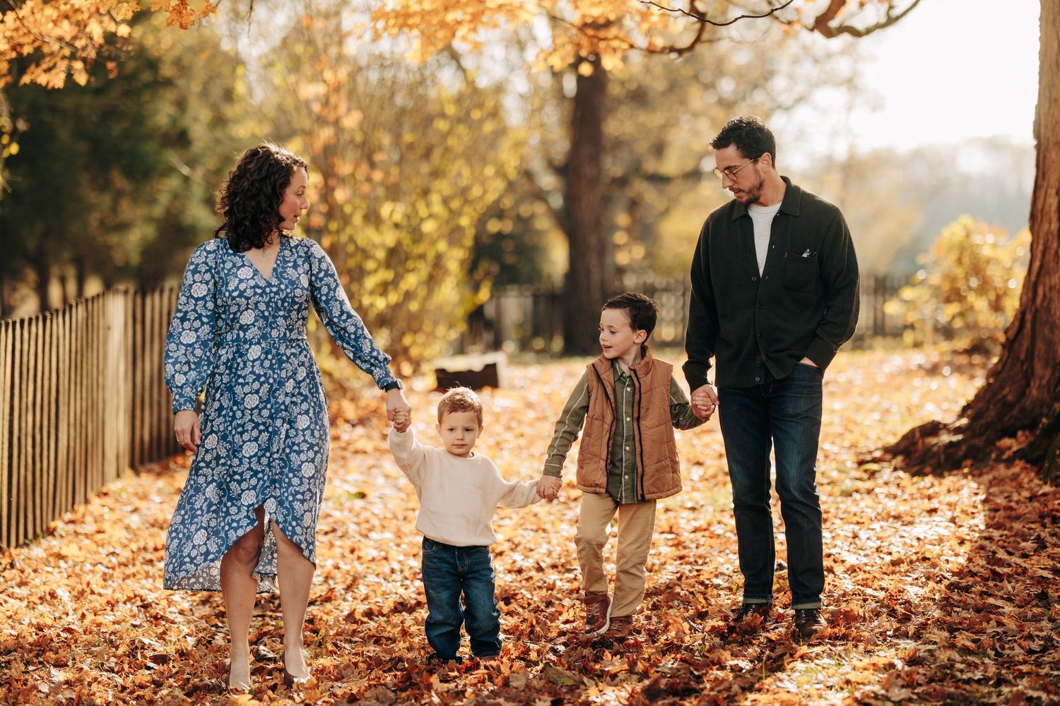 A family walks through vibrant autumn leaves on a path during a fall photo session in nature.