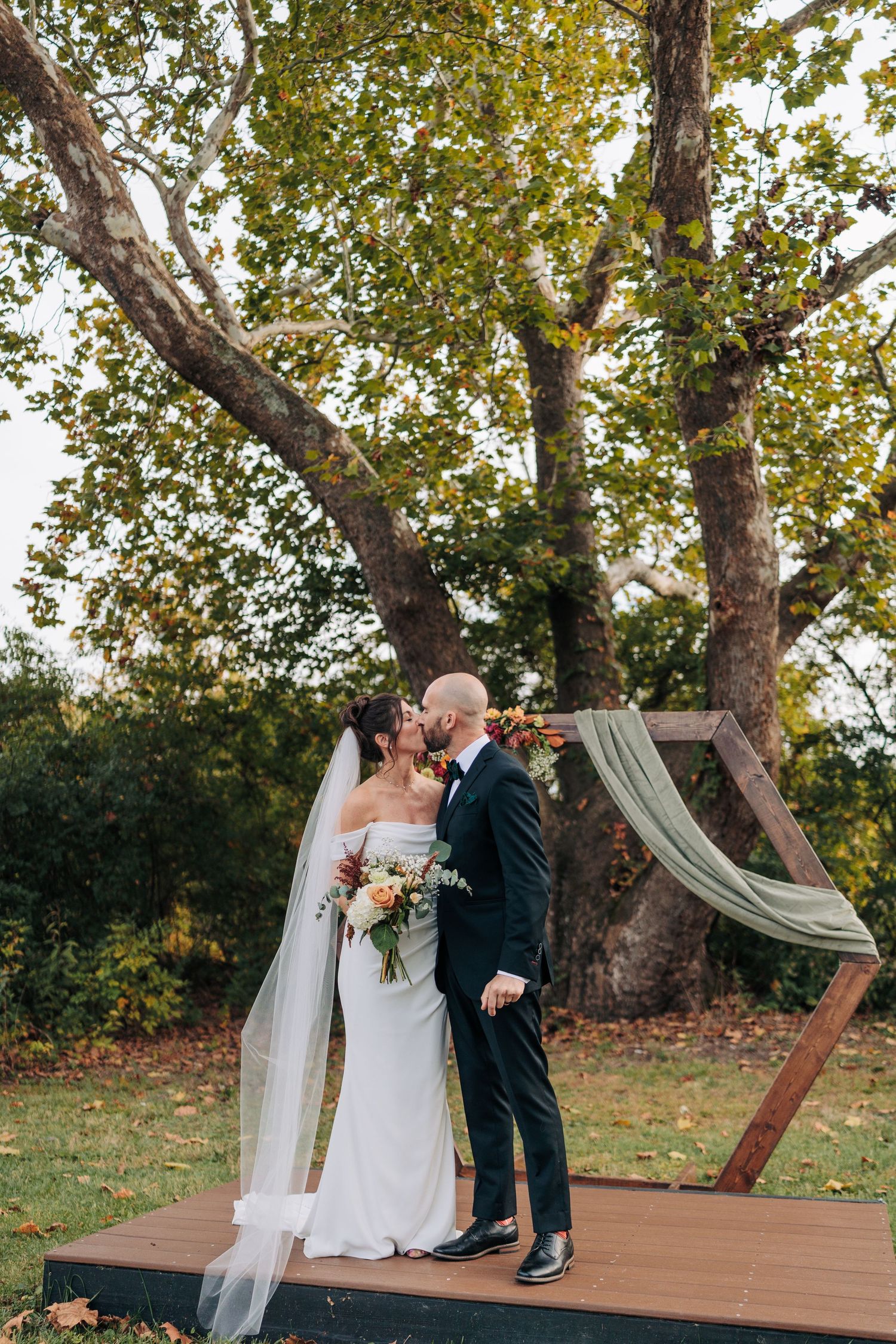 Romantic outdoor wedding ceremony on a wooden deck surrounded by autumn trees.