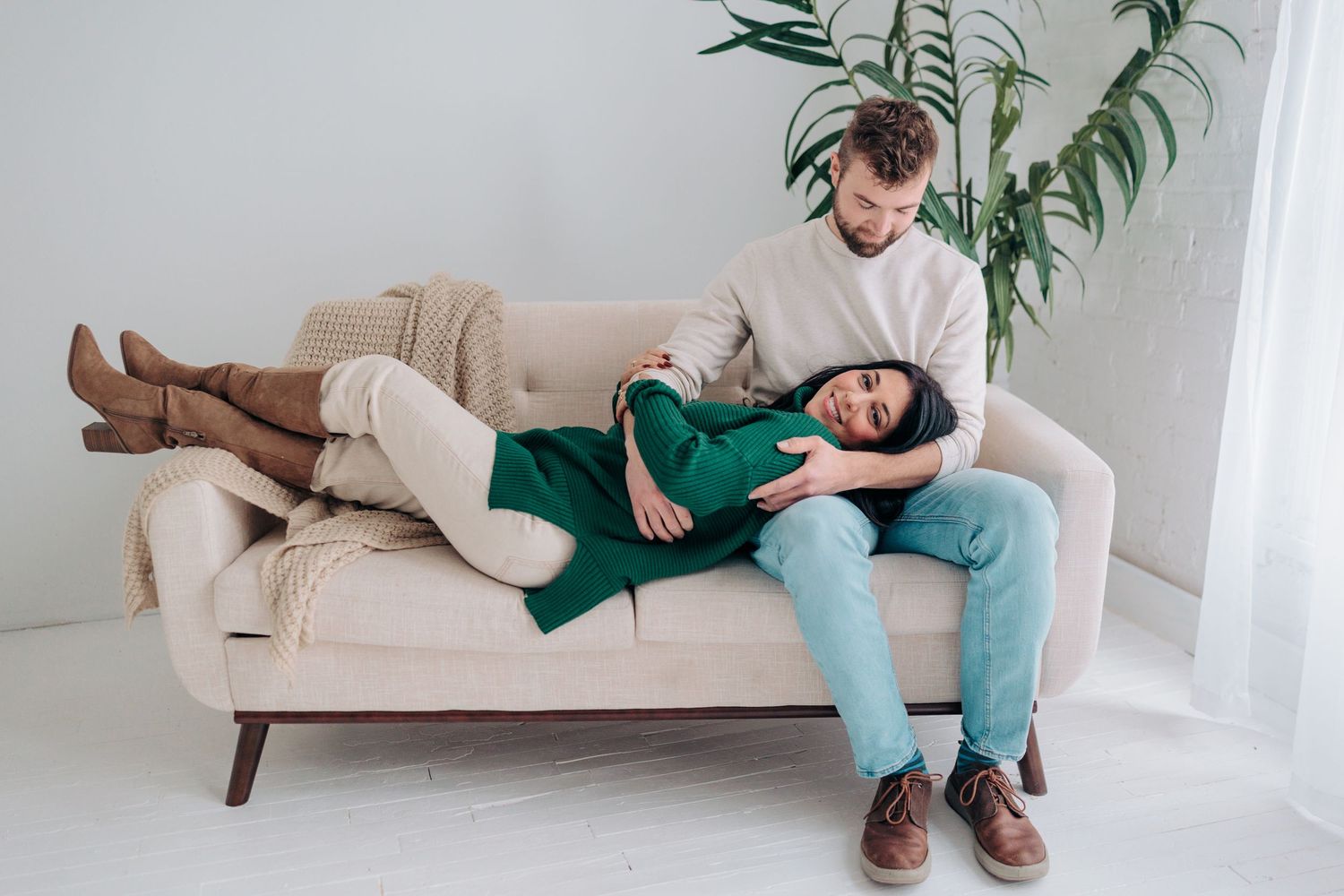 A couple relaxes together on a beige couch in a bright, minimalist living room setting.