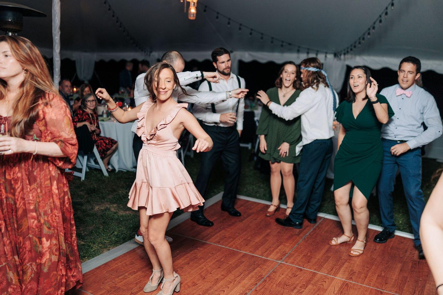 Wedding reception dance party under string lights with guests dancing on wooden floor.