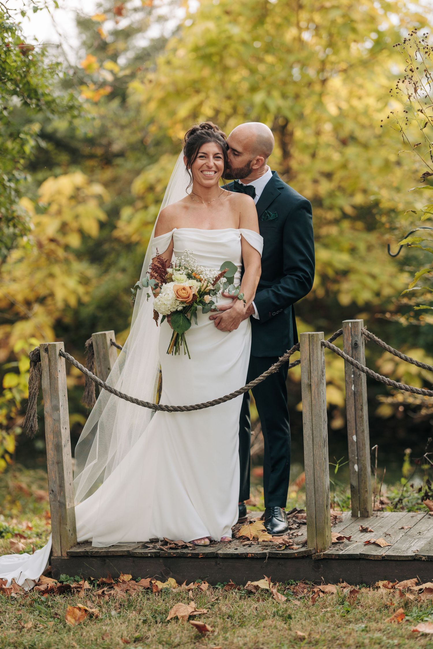 Autumn wedding photos on wooden bridge surrounded by yellow fall foliage.