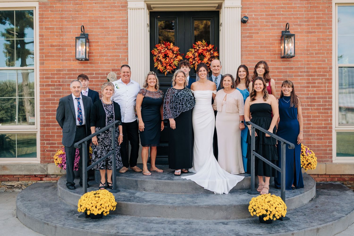Wedding party poses in front of brick building decorated with orange flowers and lanterns.