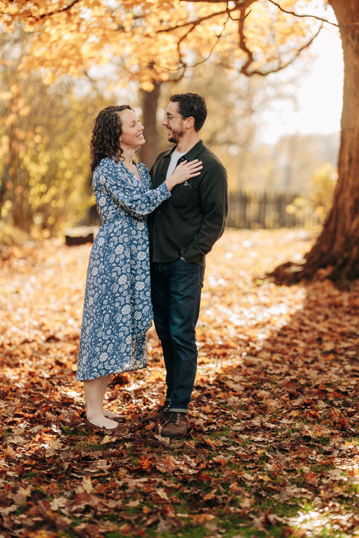 Couple sharing intimate moments among fallen autumn leaves in a park setting.
