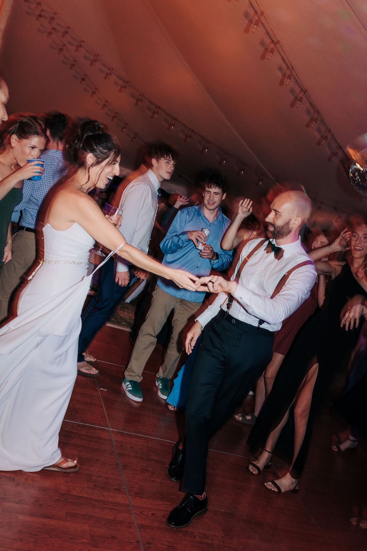 Guests dancing and celebrating on a wooden dance floor at a wedding reception with dim lighting.
