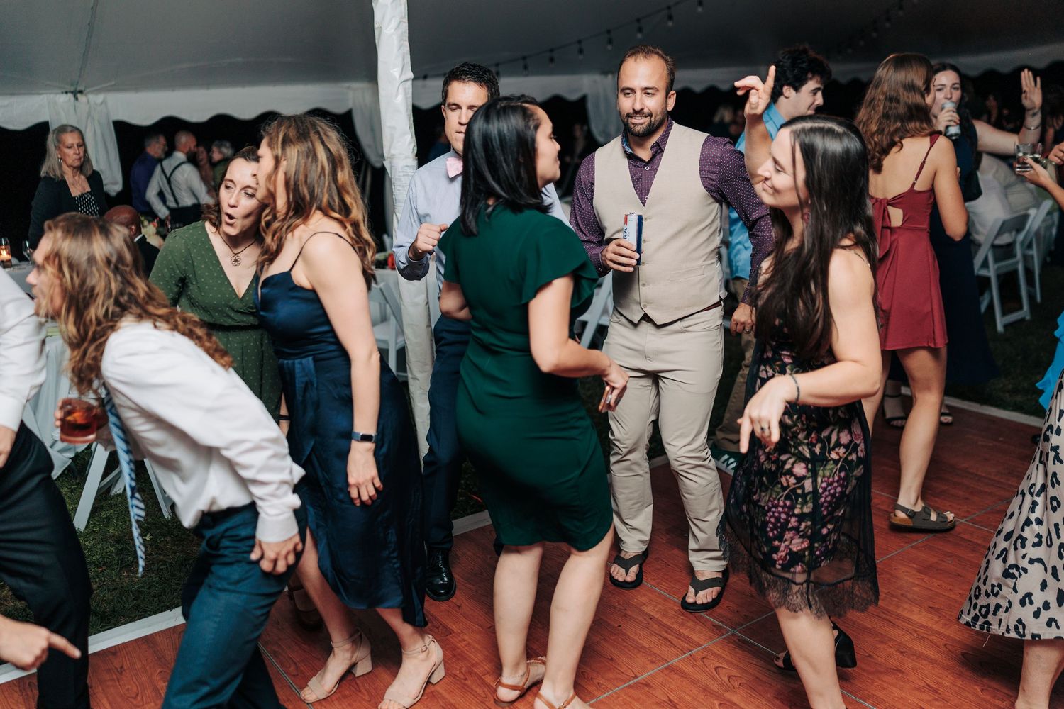 Wedding guests dancing and celebrating on a crowded dance floor under tent.