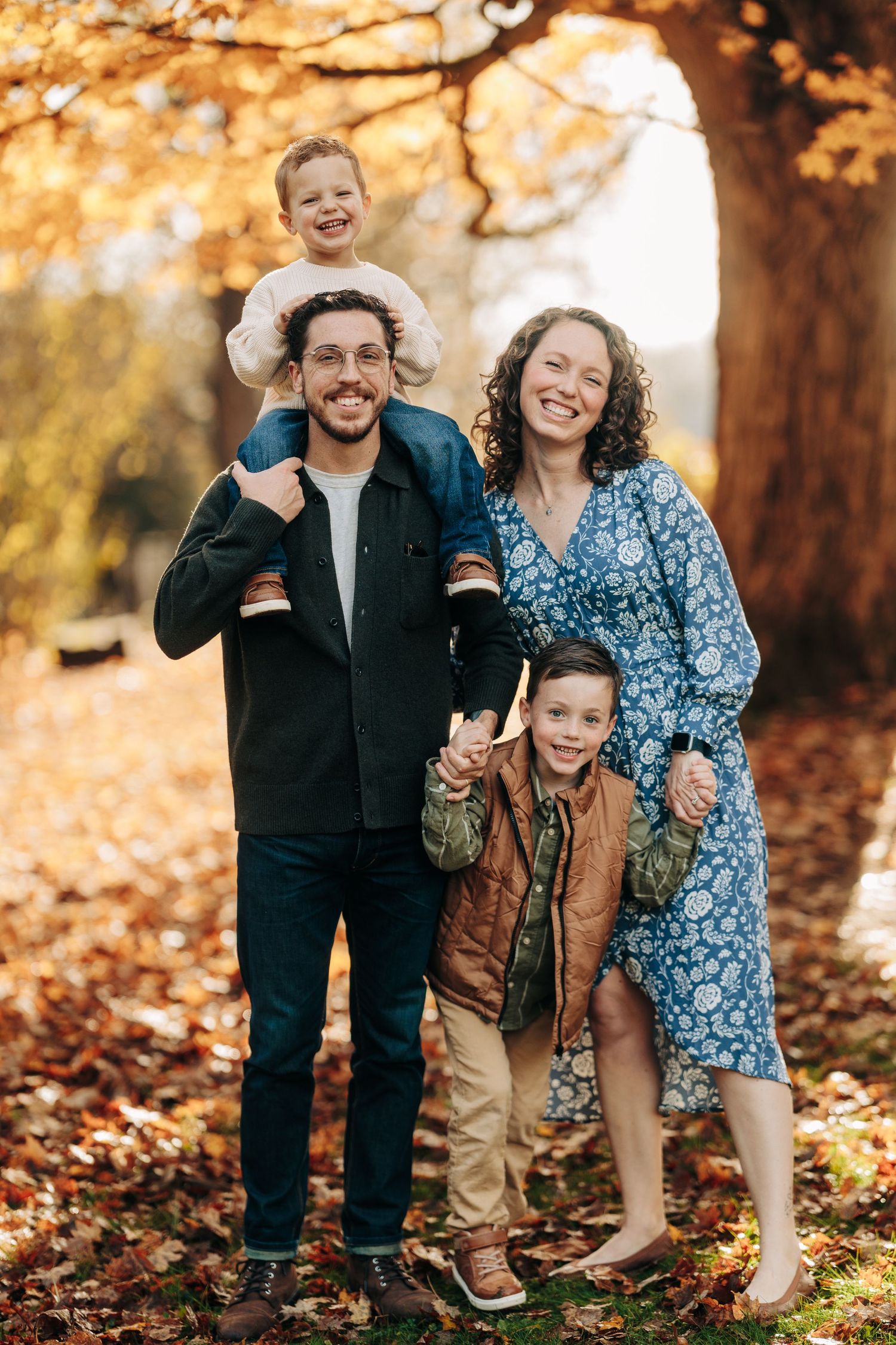 Family enjoying a playful moment together on fallen autumn leaves in a sunlit park.
