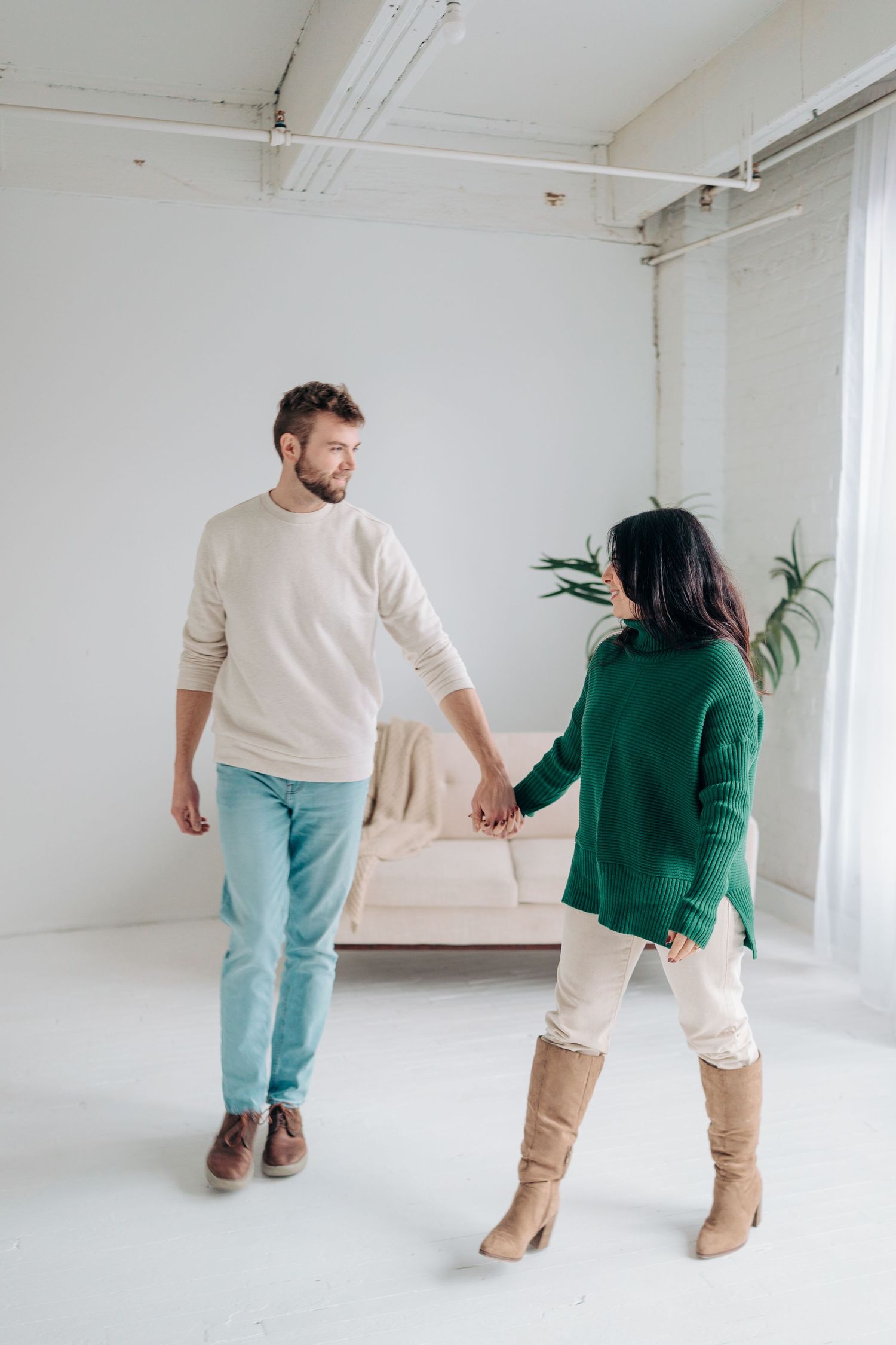 Two people in casual wear dance together in a bright white studio space with minimal decor.