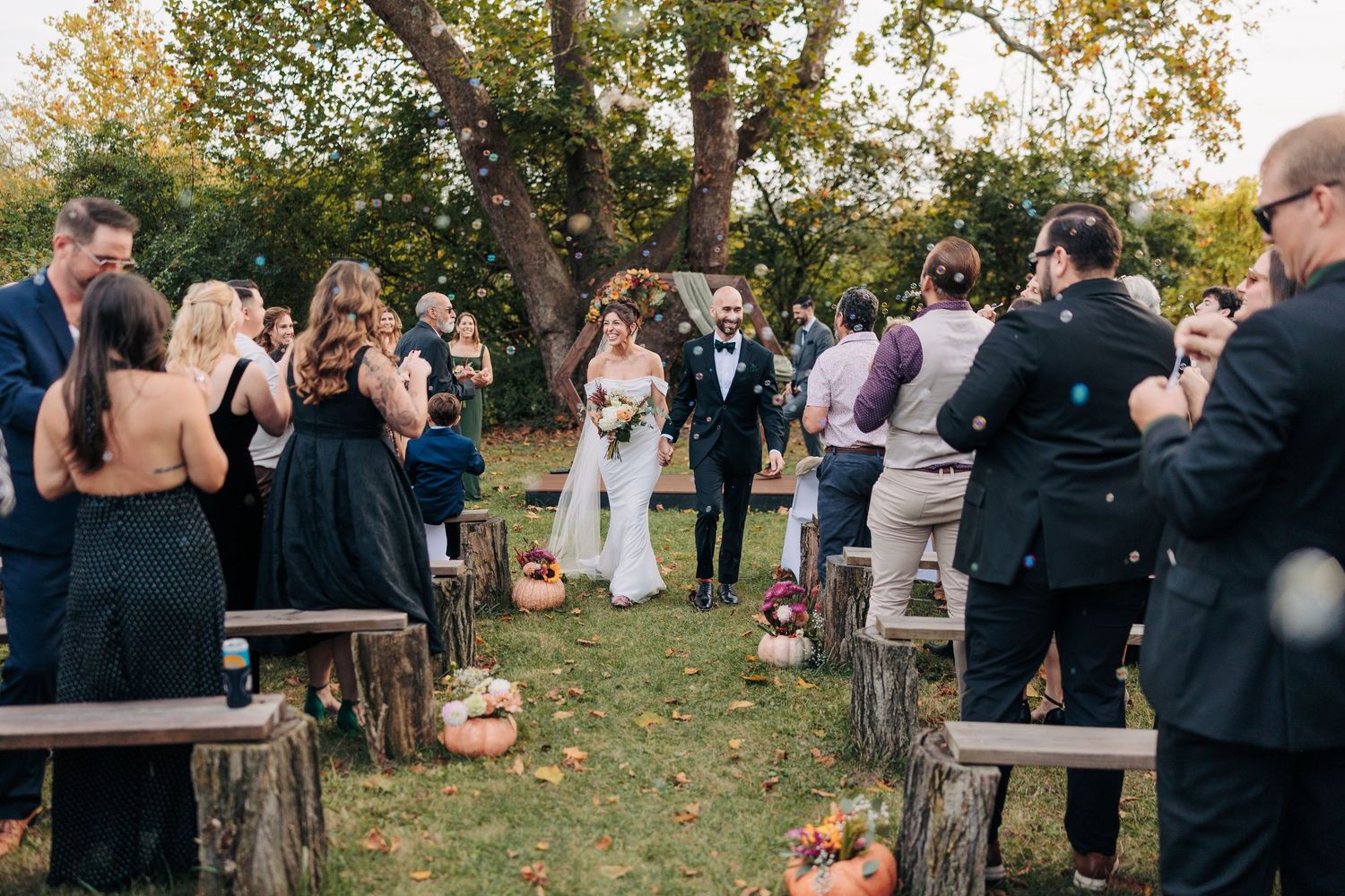 Outdoor wedding ceremony setup with rustic wooden seating and fall foliage in the background.