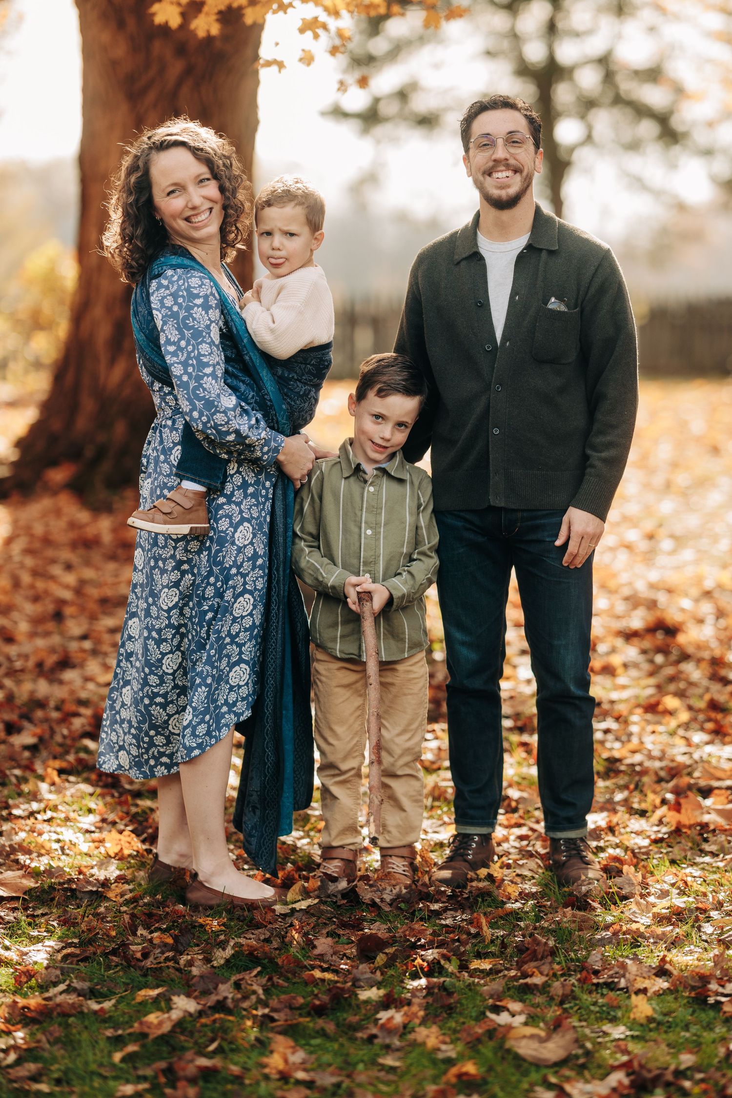 Family enjoying a fall photoshoot together among colorful autumn leaves scattered on the ground.
