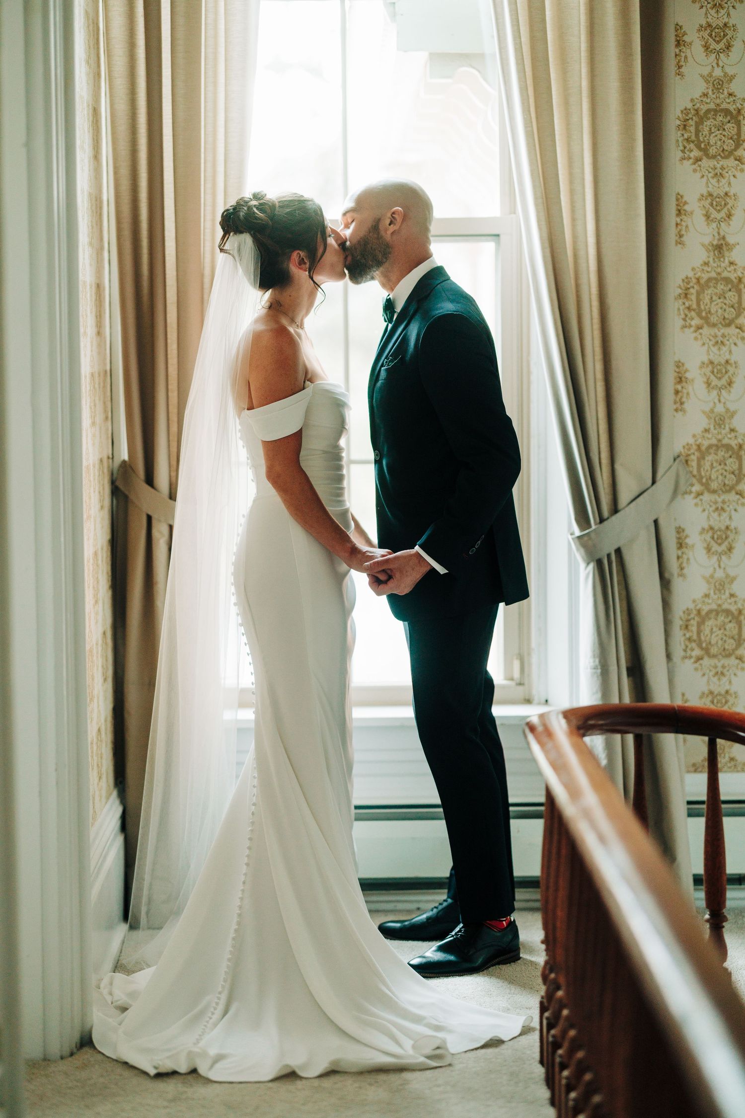 Elegant indoor wedding portraits showing couple in formal attire against light curtained windows.