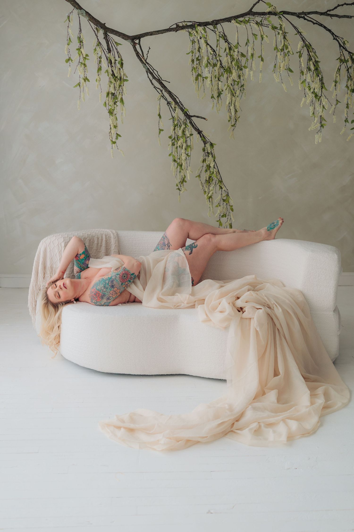 A dreamy maternity photo series shows a figure in white reclining on a soft backdrop beneath willow branches.