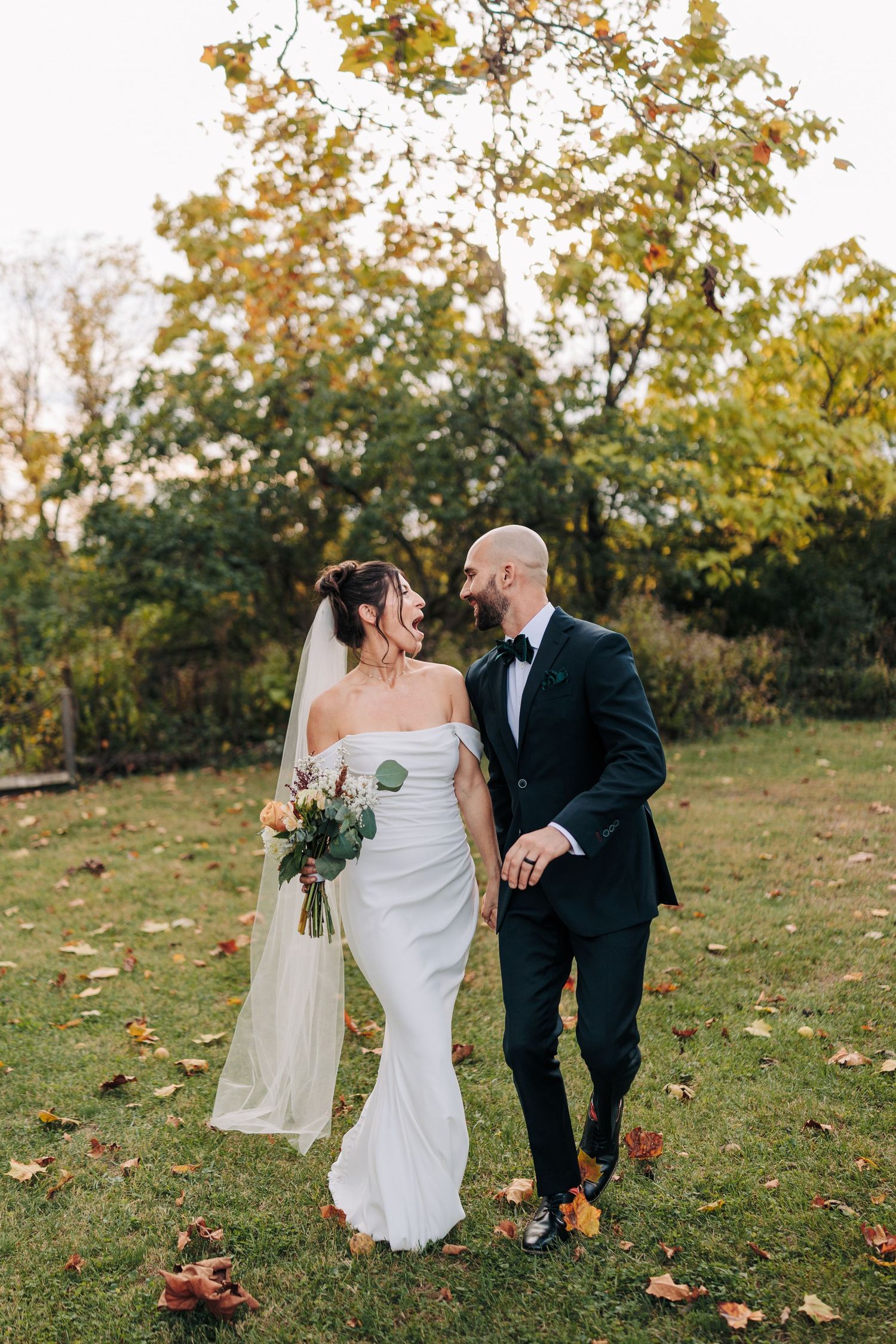 Wedding couple walking together on grassy hill during fall season.