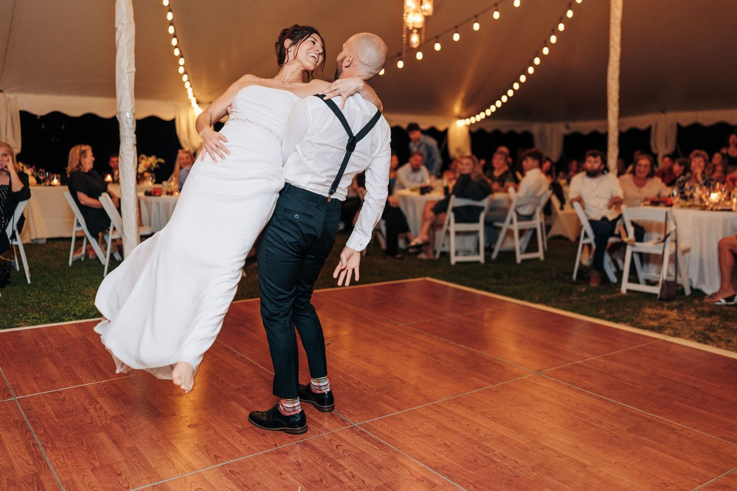 Wedding reception dancing under string lights in a tent with wooden dance floor.