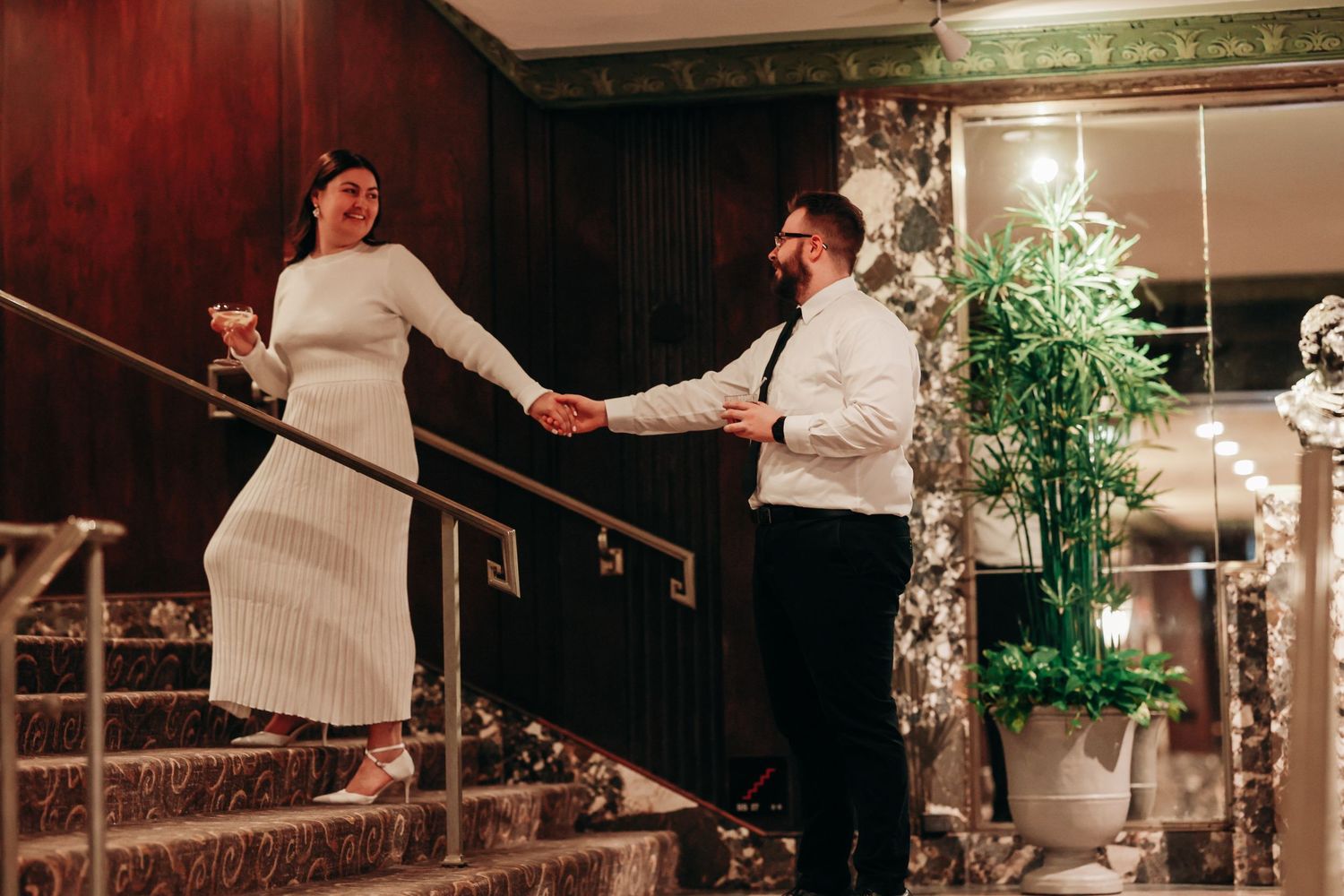 A couple holding hands on elegant wooden stairs during a romantic moment.