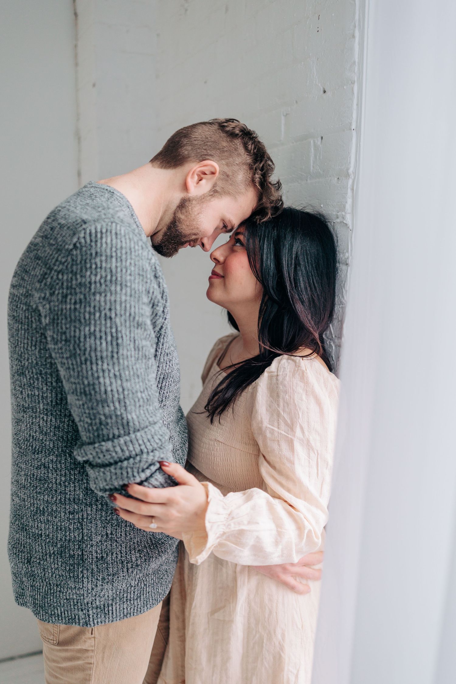 Two people share an intimate moment while wearing cozy sweaters in a bright white room.