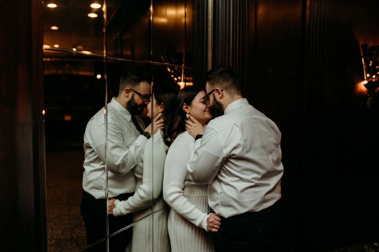 A romantic moment reflected in mirrors with warm lighting and formal attire.