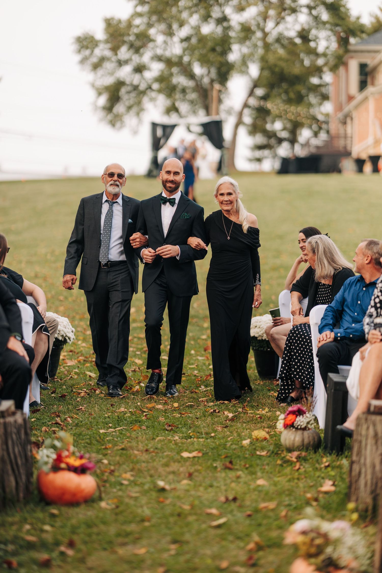 Wedding guests gather on a grassy hillside with pumpkin decorations during fall ceremony.