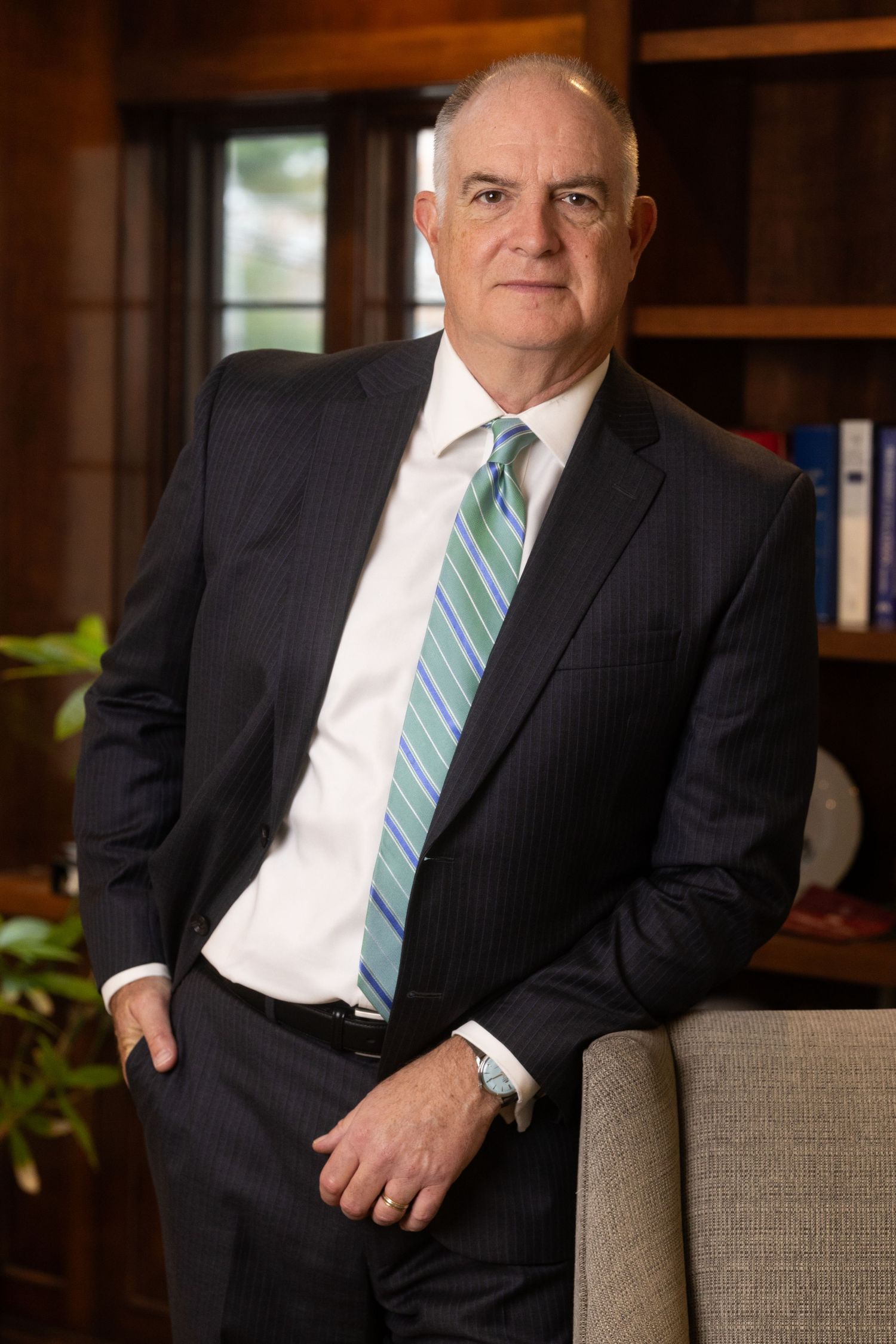 Business professional in pinstripe suit seated on grey office chair during corporate photoshoot.