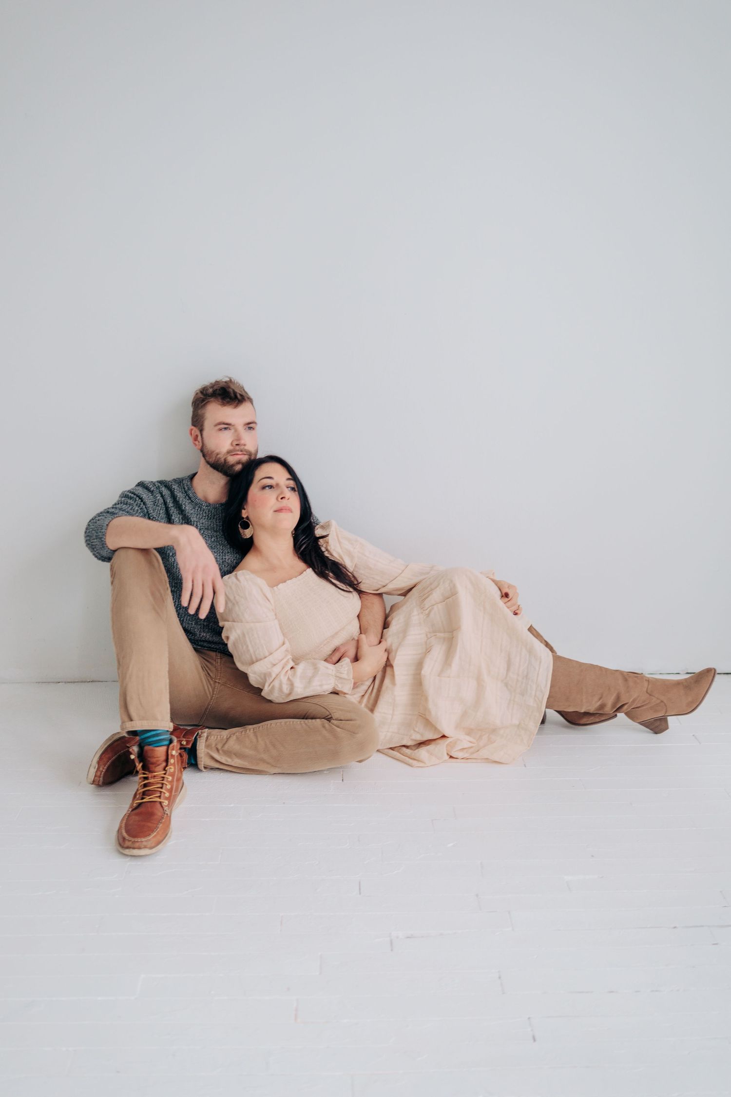 Two people in casual attire lying on white floor in minimalist setting for artistic portrait series.