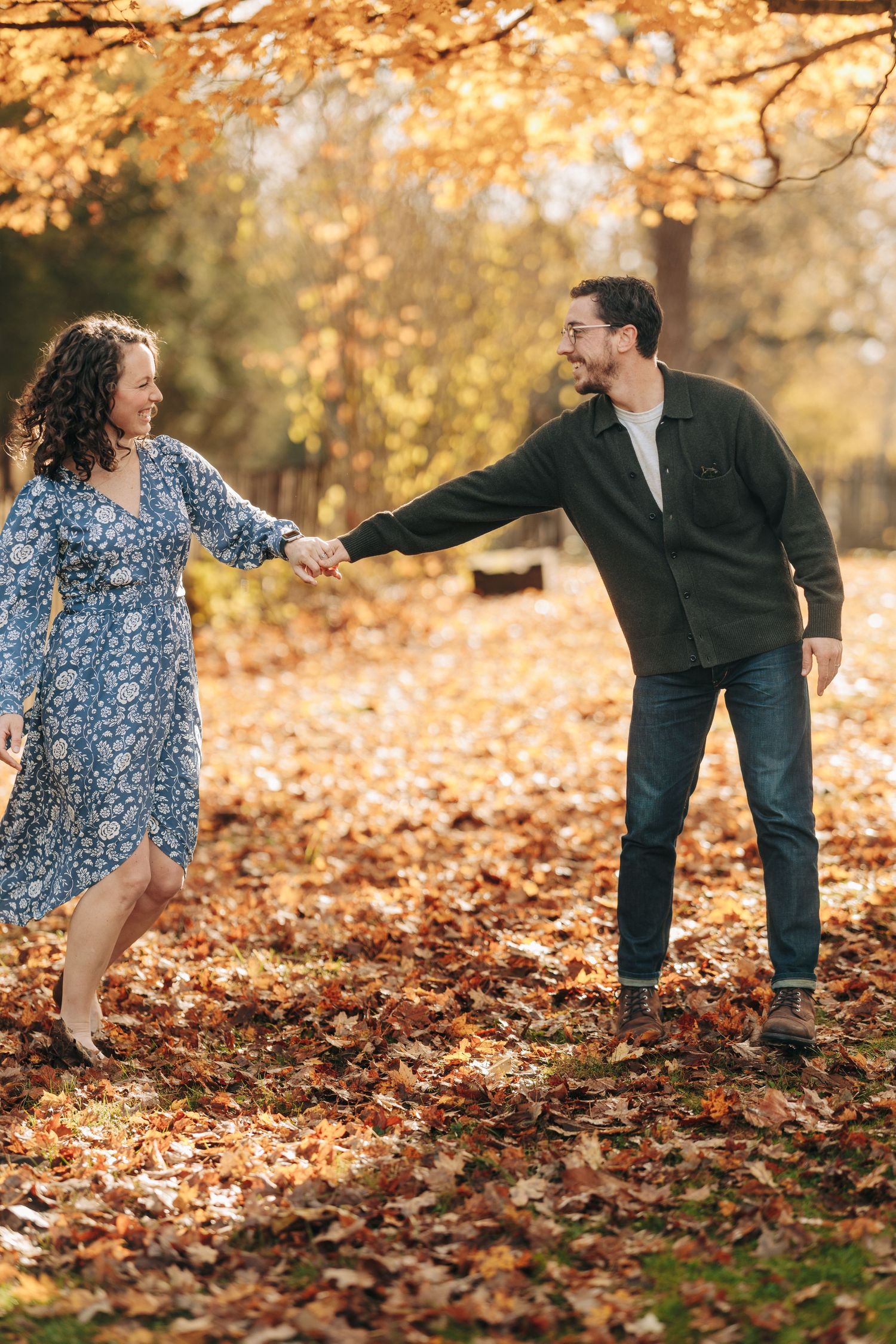 A couple playfully interacts in autumn leaves during a romantic fall photoshoot in golden sunlight.