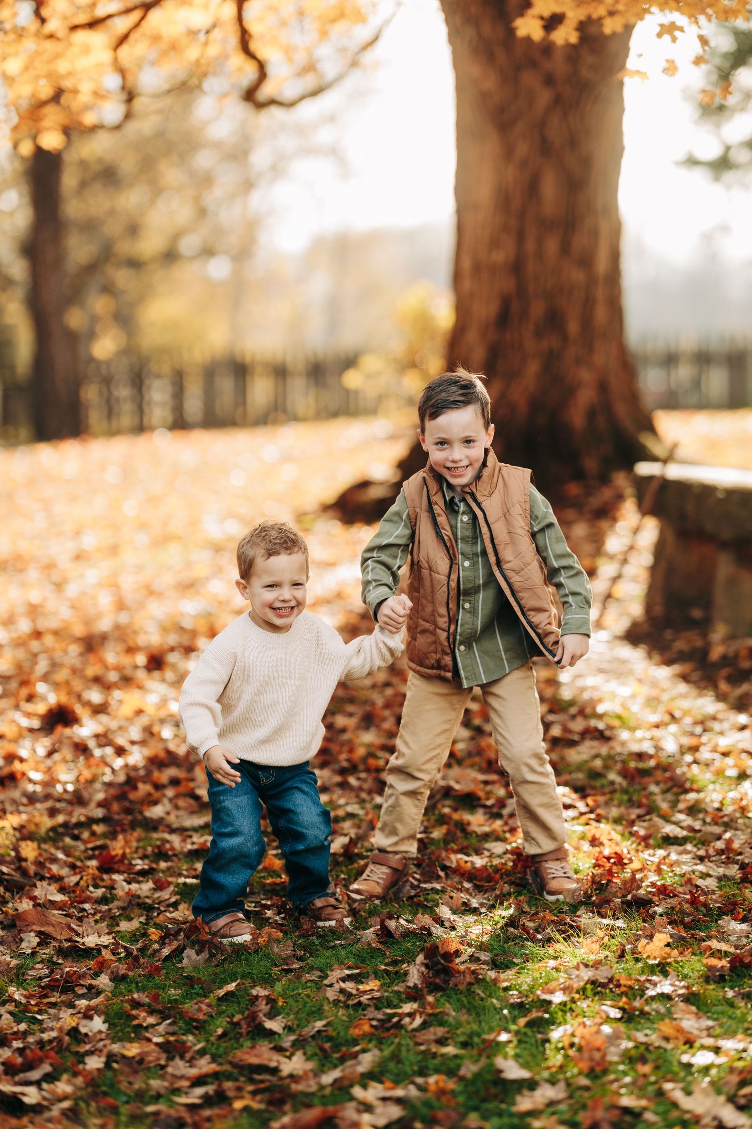 Two children playing and laughing together among fallen autumn leaves in a park on a golden fall afternoon.