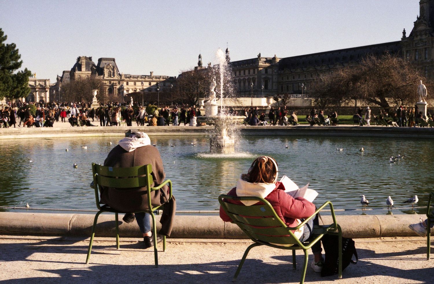 Photo de rue à l'argentique. Des parisiens sont installés au soleil dans le jardin des tuileries un jour d'hiver