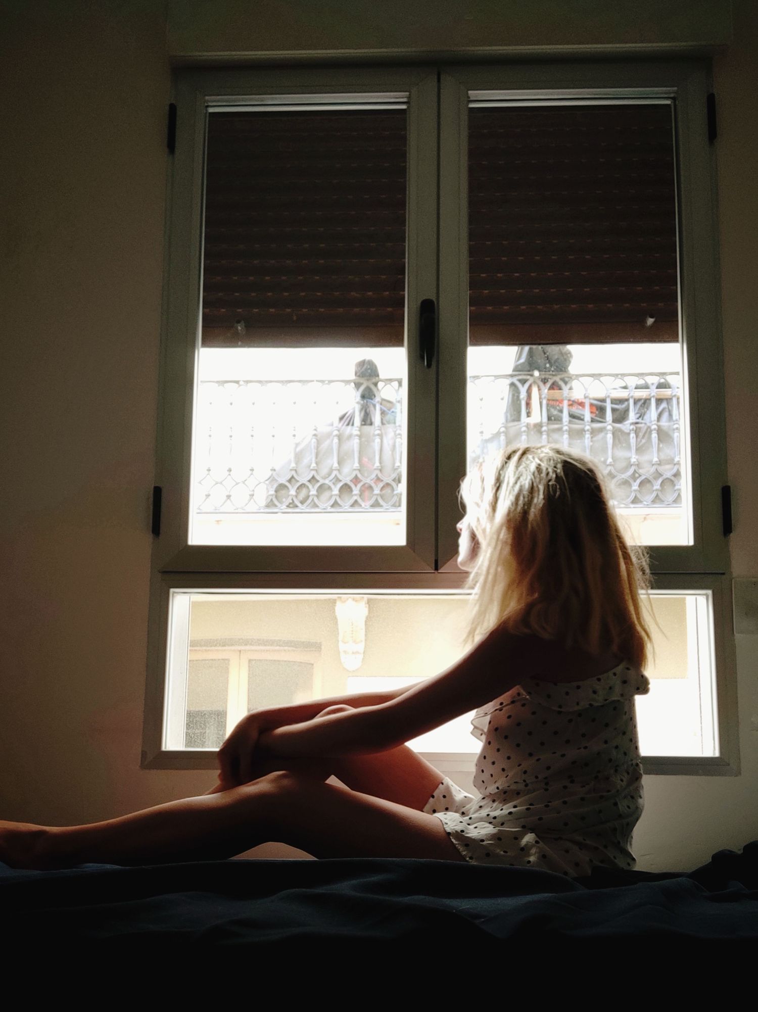 Autoportrait d'une femme assise en contre jour, regardant vers l’extérieur, une fenêtre derrière elle.
