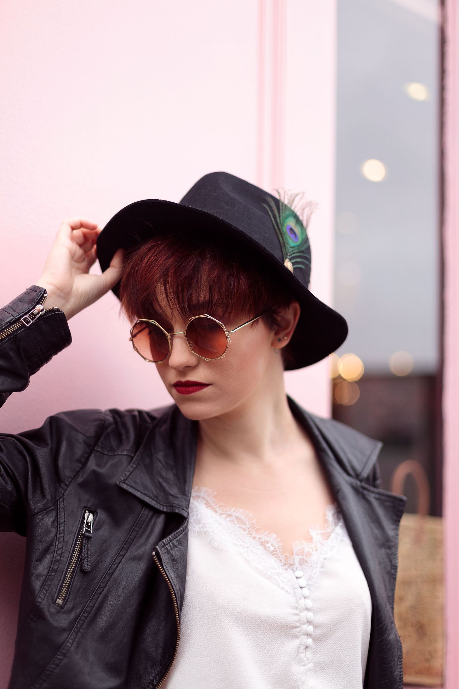 Portrait d'une femme portrant un chapeau et des lunettes de soleil devant un fond rose pale