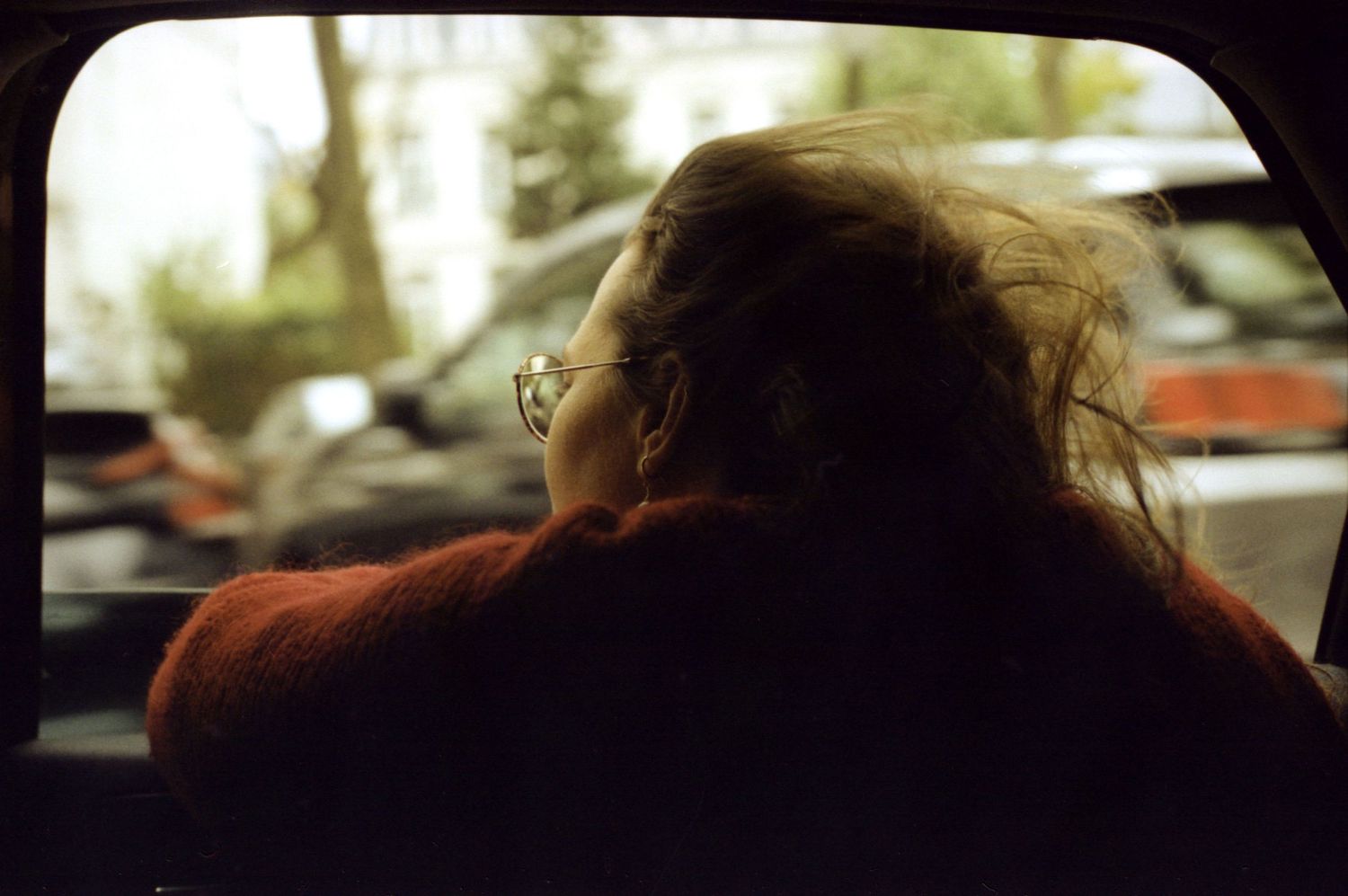 Portrait argentique d'une femme regardant par la fenêtre d'une voiture, cheveux au vent.
