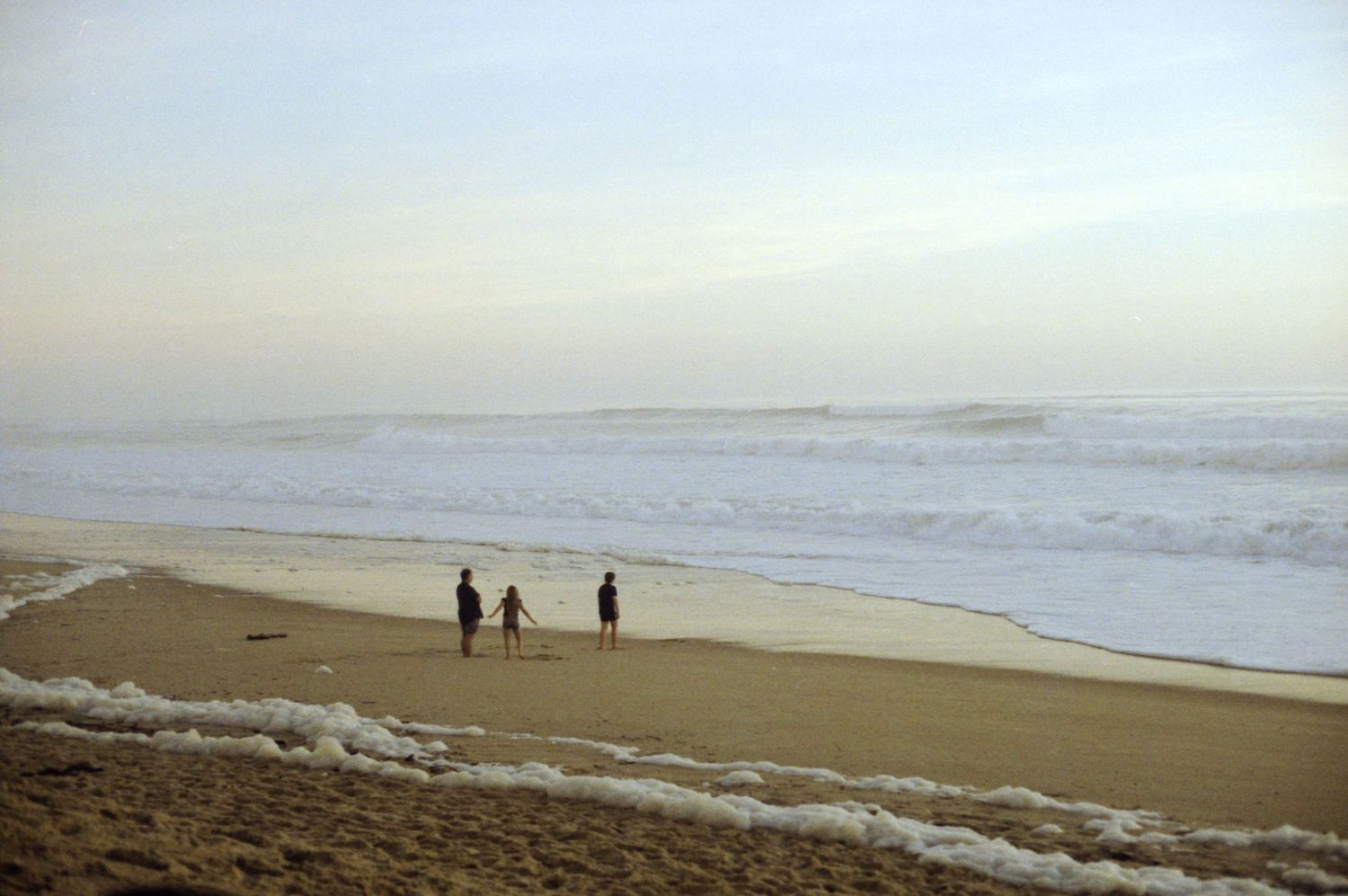 Photo argentique de 3 personnes sur une plage déserte, jouant avec l'écume des vagues.