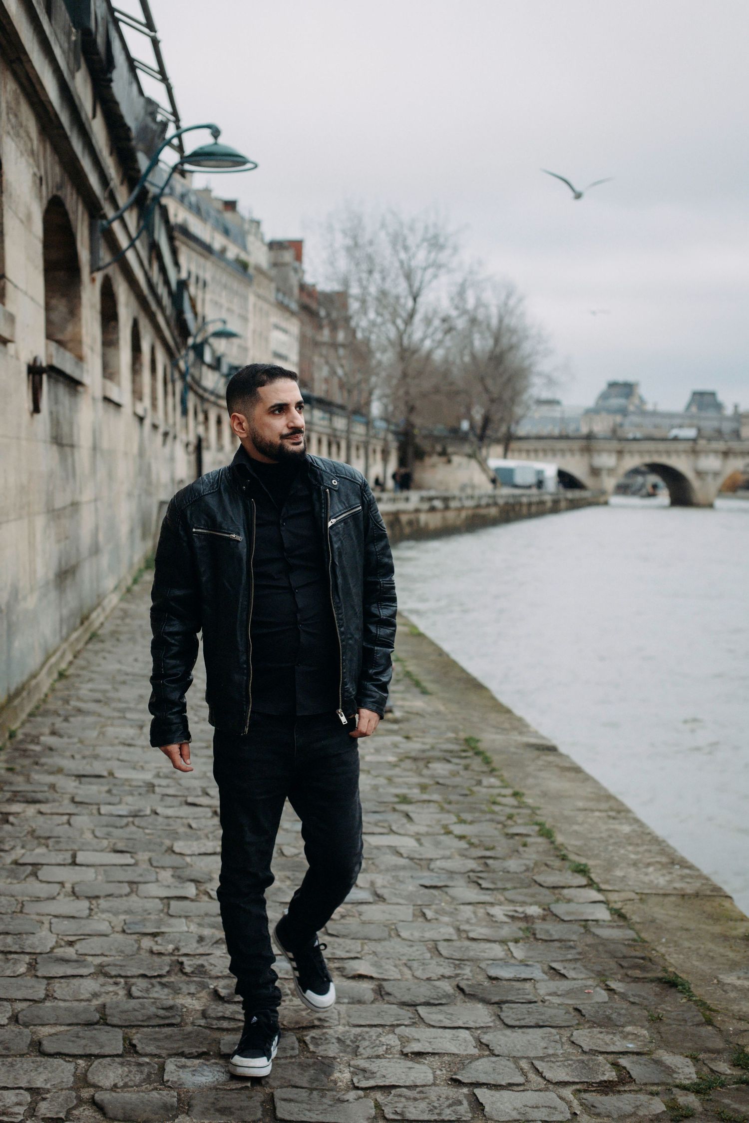 Portrait d'un homme brun qui se promène sur les quais à Paris, par temps nuageux.