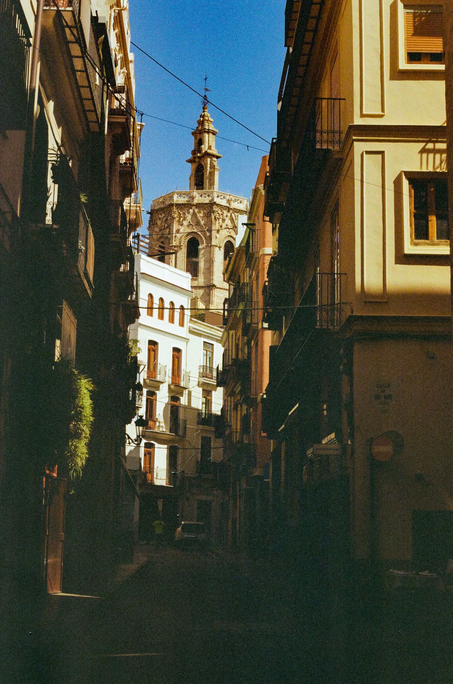 Photo de rue à l'argentique du centre ville de Valencia. Les rues étroites sont en clair-obscur et au loin un clocher surplombe.