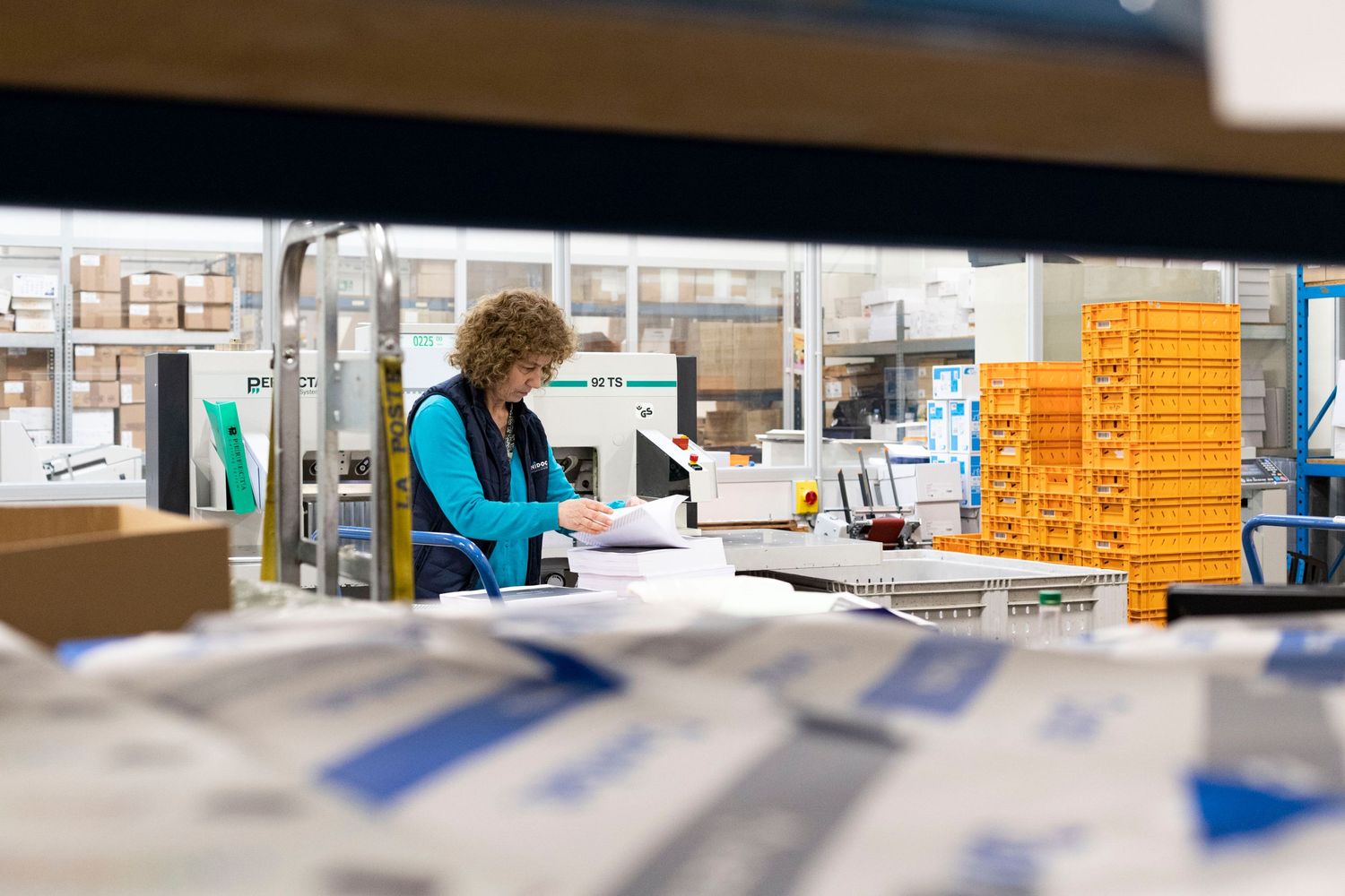 Photographie de reportage prise au sein d'une imprimerie. Une femme s'occupe de la logistique entourée de piles de papier