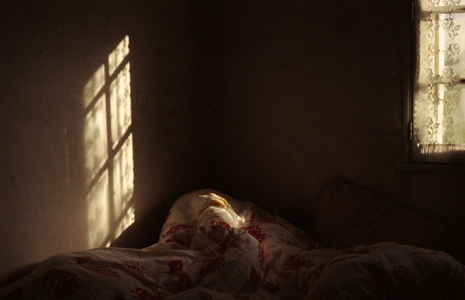 Photo argentique d'une chambre dans la pénombre, le soleil illuminant uniquement la projection des vitres de la fenêtre.