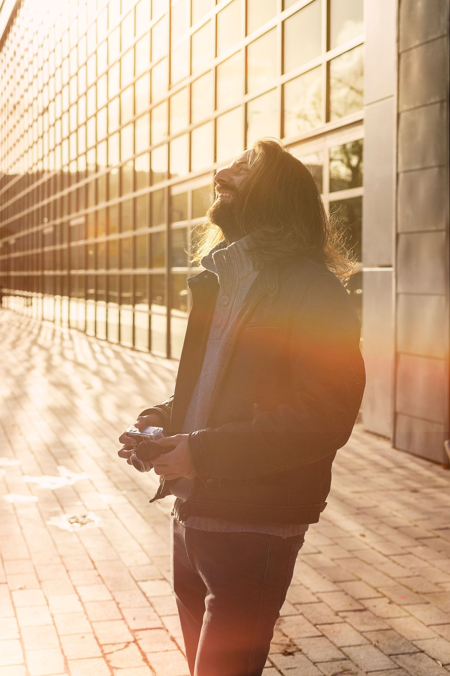 Portrait d'un homme qui ris au éclat, un appareil photo dans les mains, dans un environnement urbain.