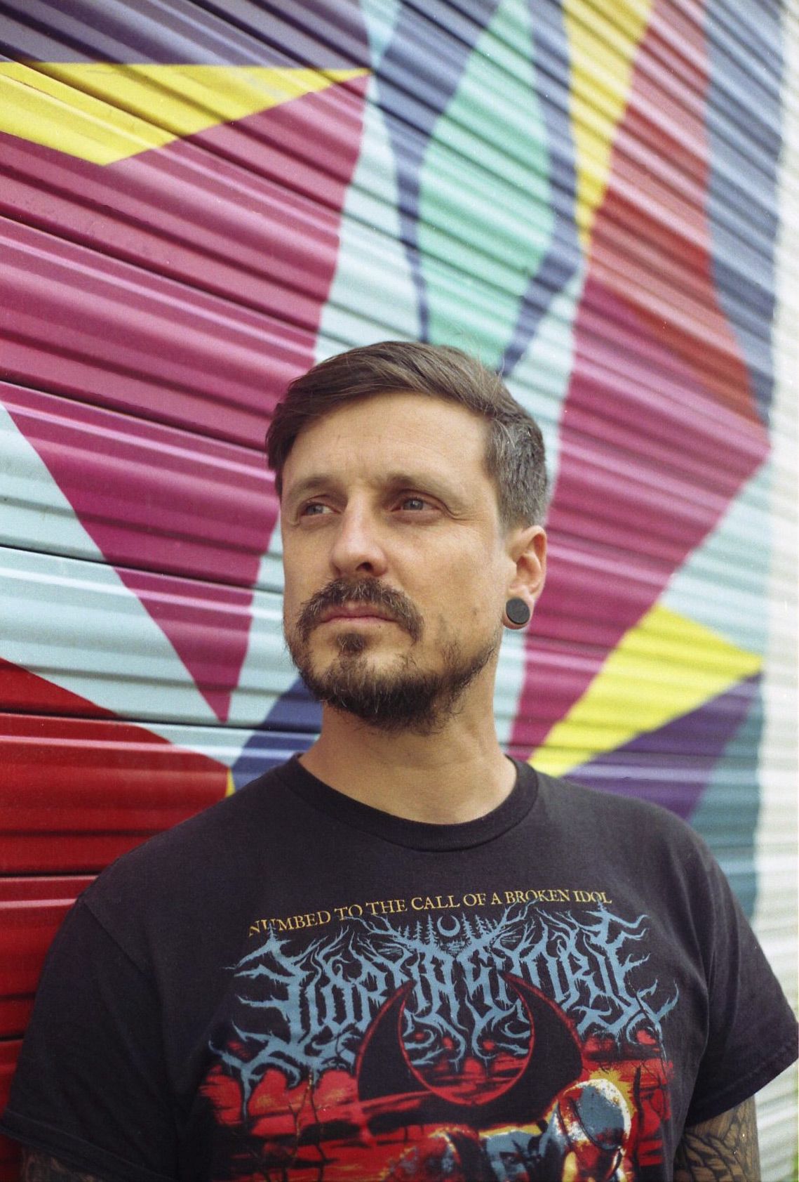 Portrait à l'argentique d'une homme devant un store métallique avec du street art coloré
