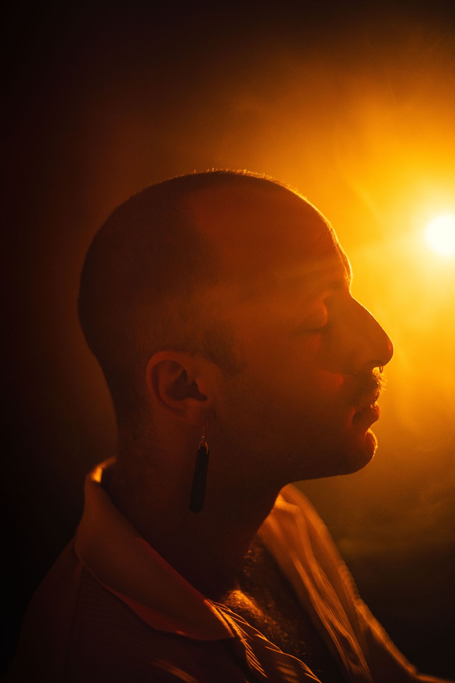 Portrait d'un homme de profil, une lumière orangée et de la fumée derrière lui