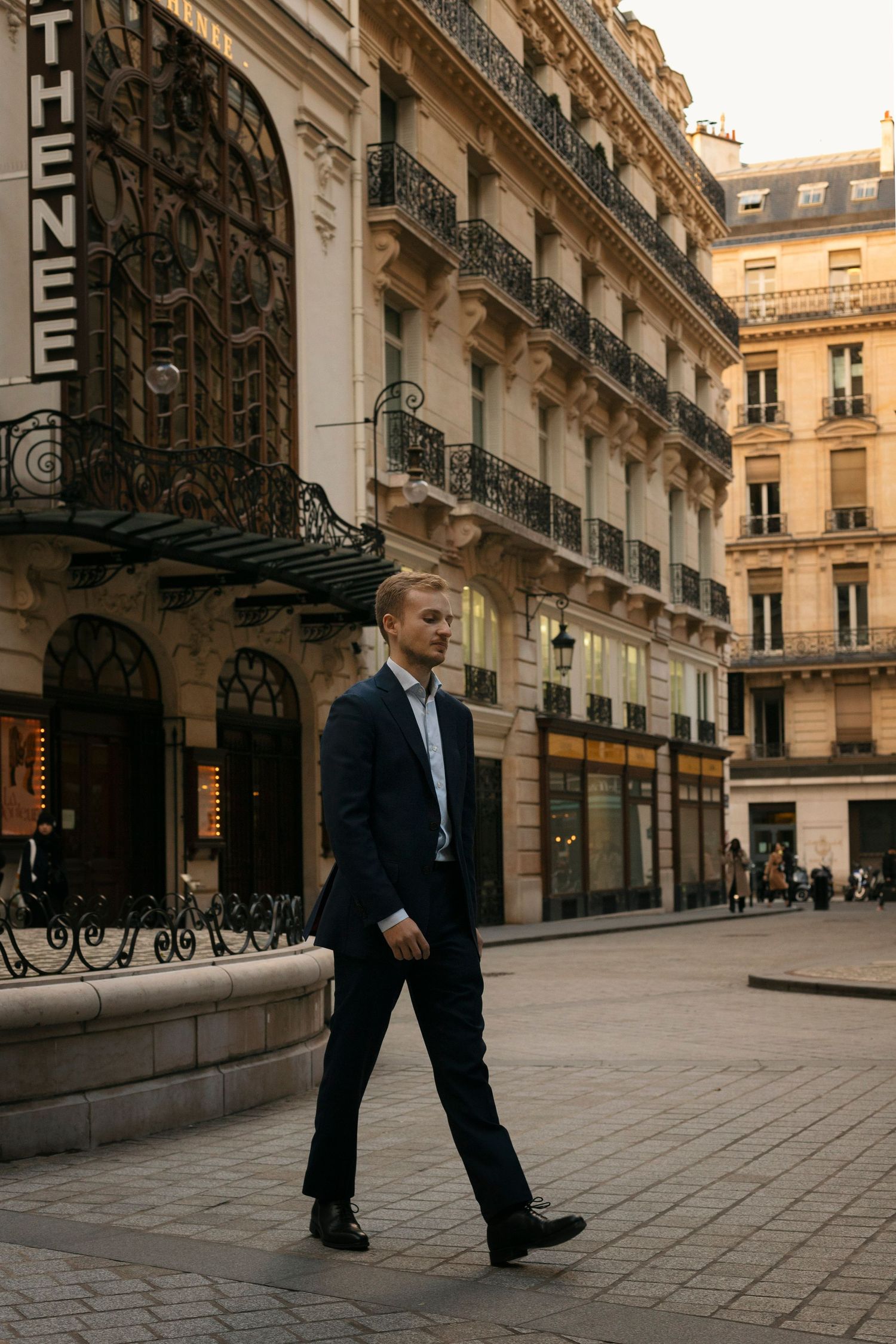 Photo d'un homme en costume marchant devant des immeubles haussmanniens.