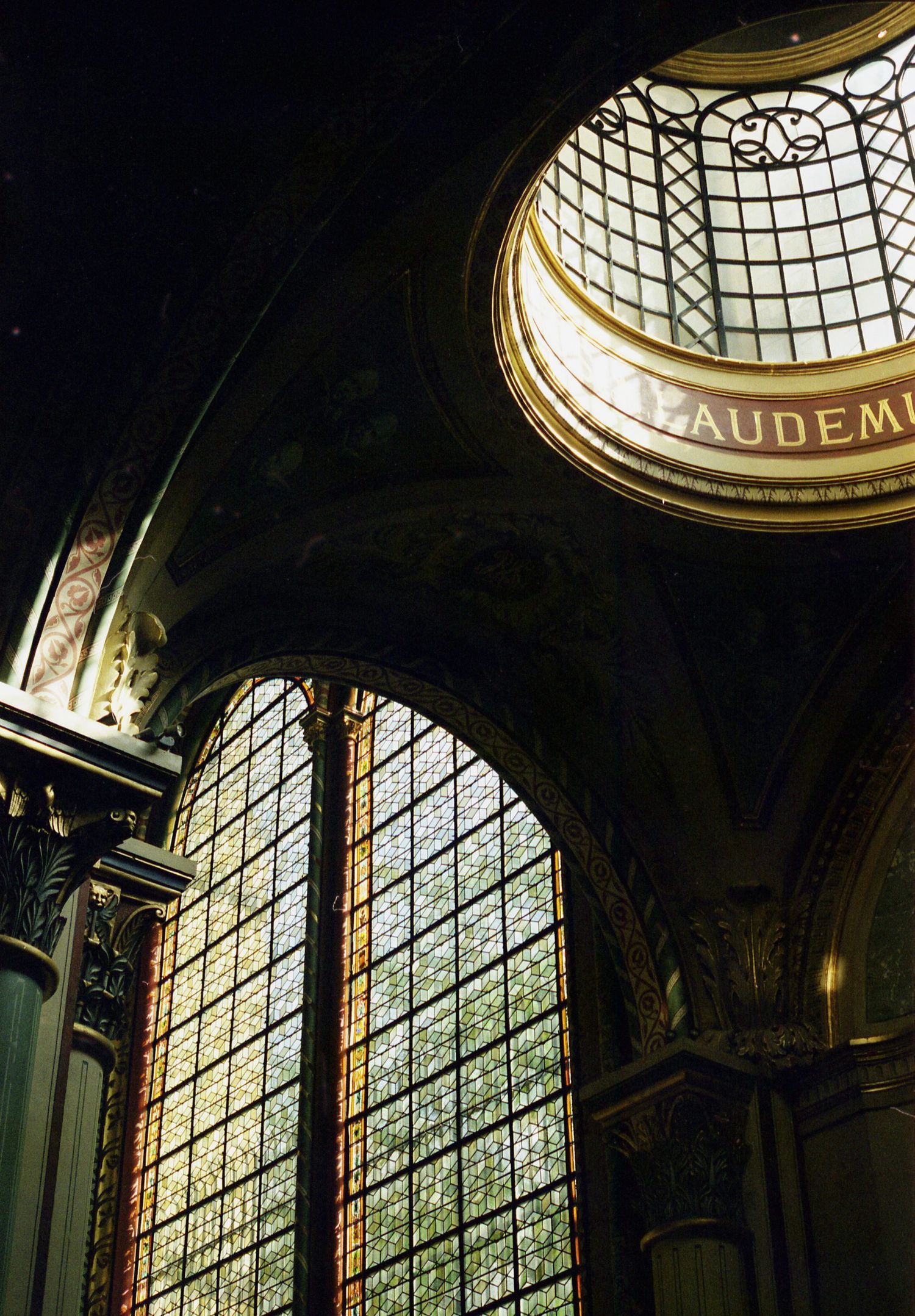 Photo argentique de l'intérieur d'une église en clair obscure. L'ensemble est sombre sauf la coupole et le vitrail qui sont illuminés.