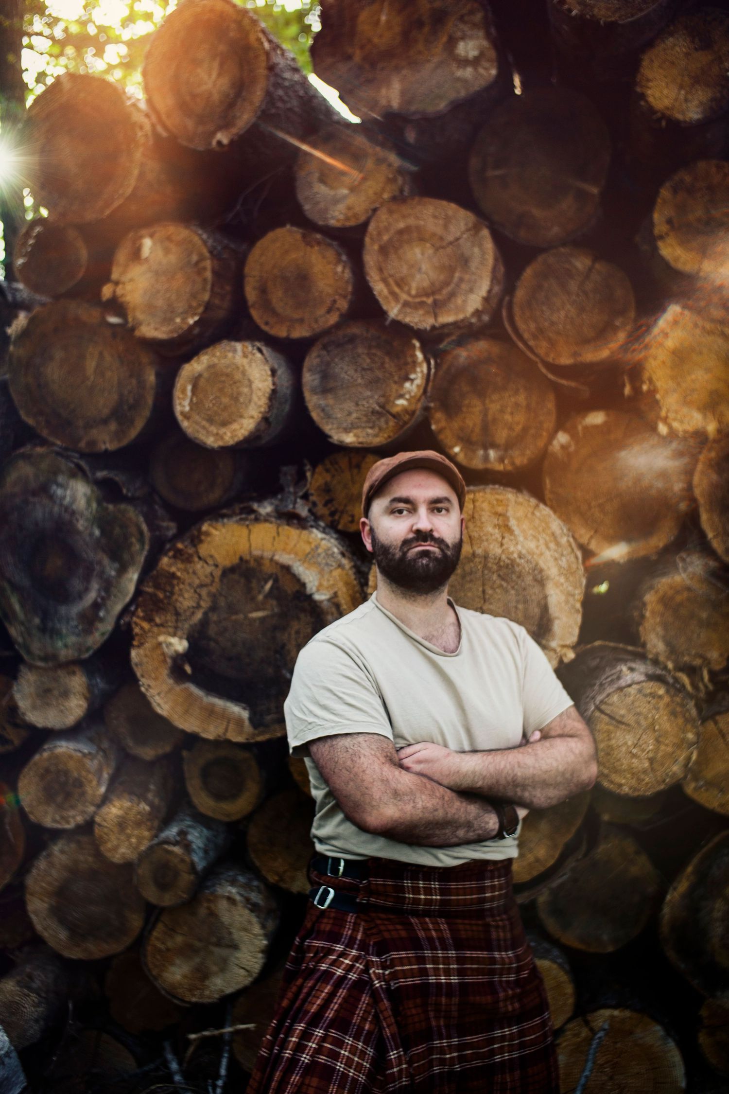 Portrait d'un homme barbu et en kilt posant devant un tas empilé de tronc d'arbre